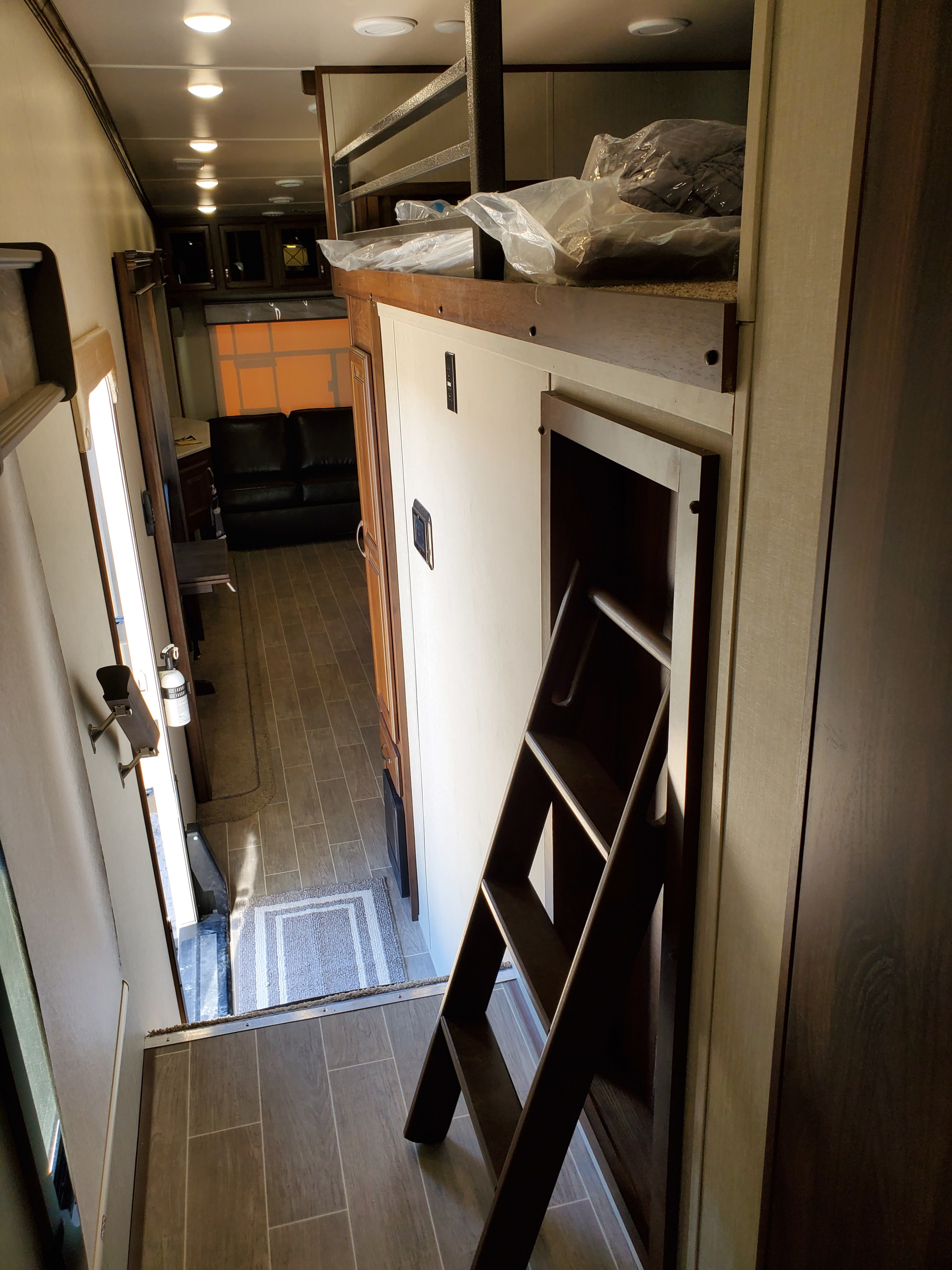 Inside an RV rental: View of a hallway with a ladder leading to a loft bed, extending to a living area with a dark sofa.. Palomino Columbus 2019