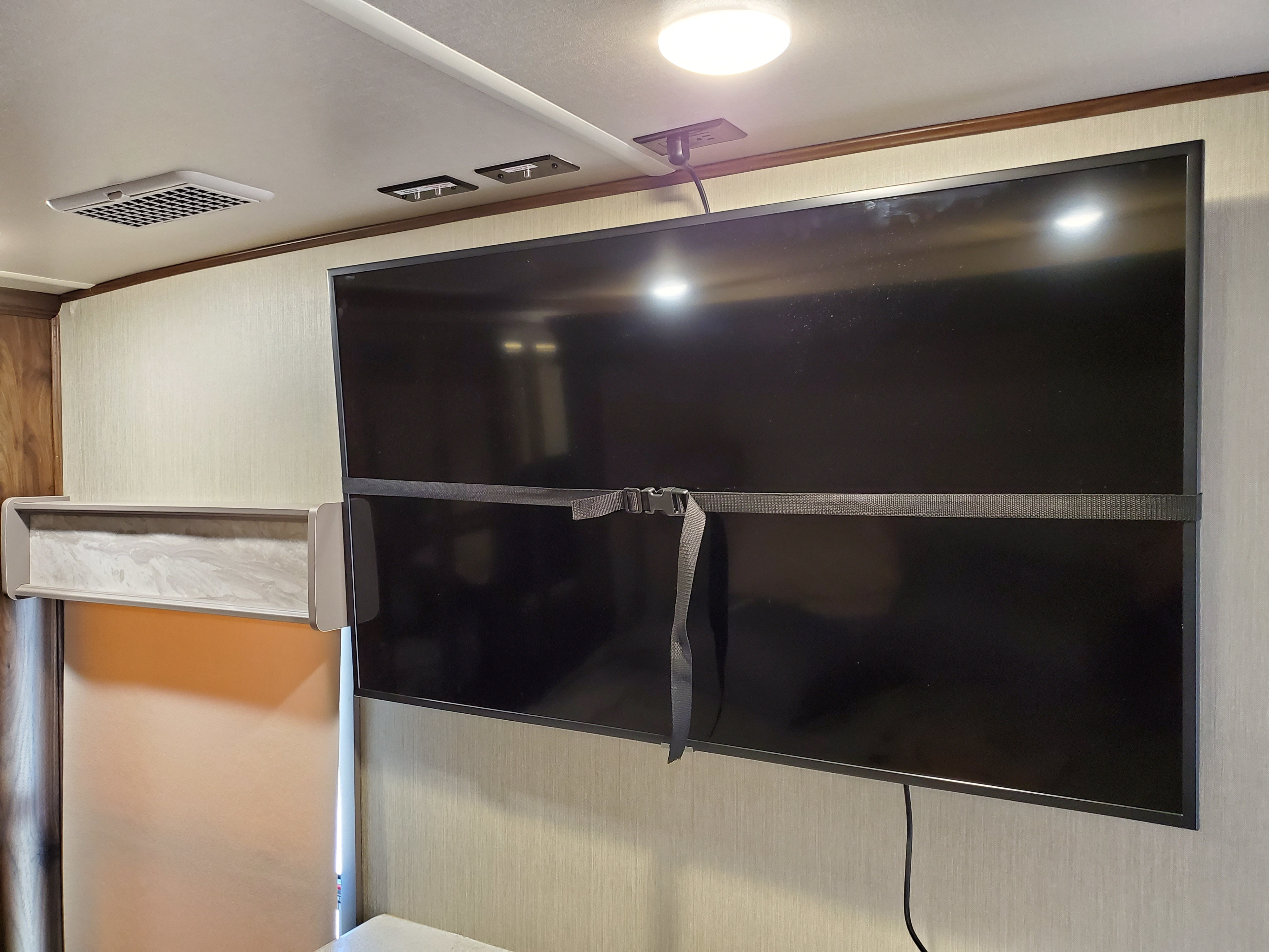 RV rental interior features a large TV, secured by a strap for travel, with an overhead light, power outlet, and ceiling vent.. Palomino Columbus 2019