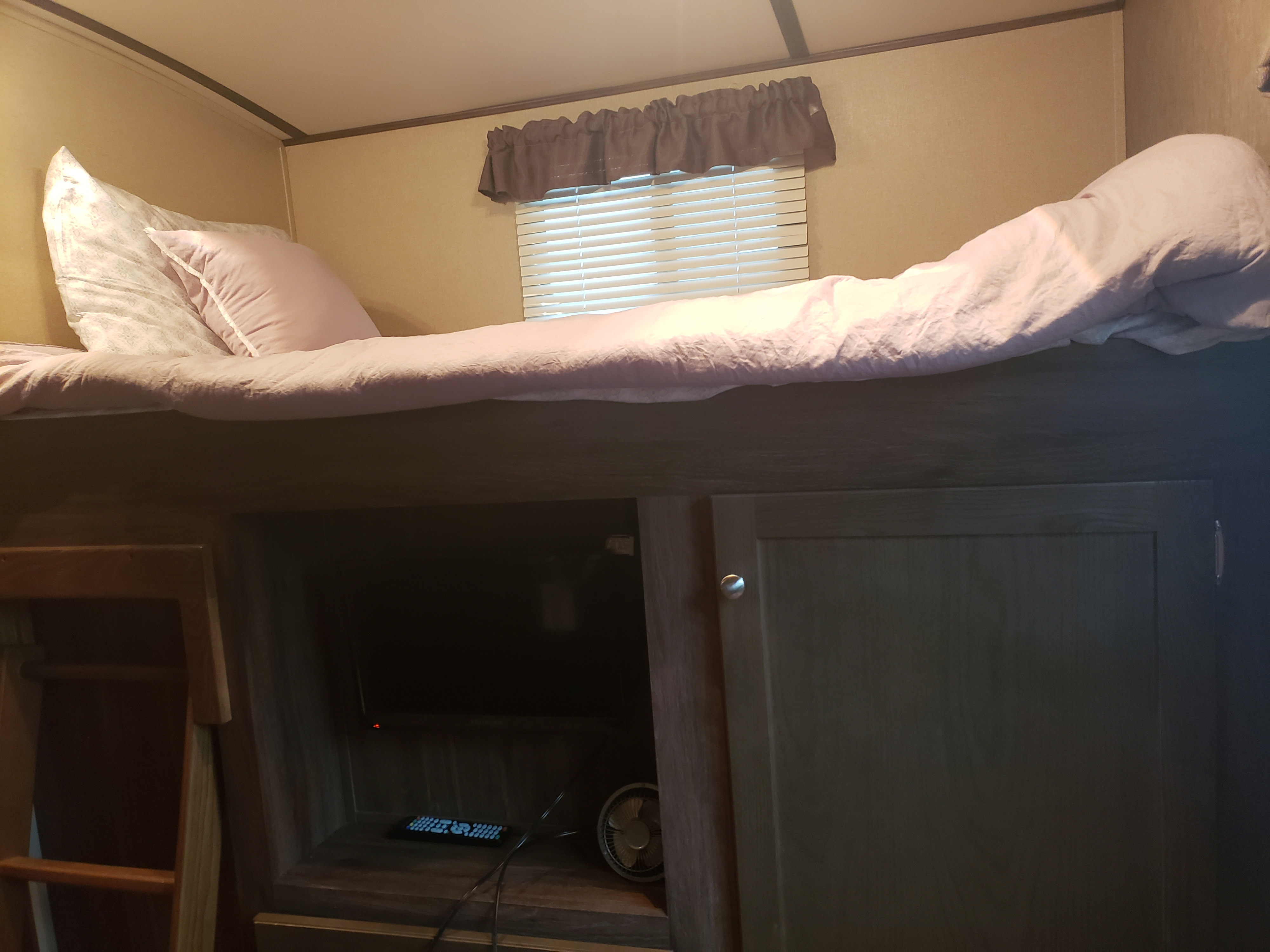 Cozy RV rental bunk bed, showing pink bedding & pillows. Below, a TV, remote, & fan provide entertainment.. Dutchmen Aerolite 2016
