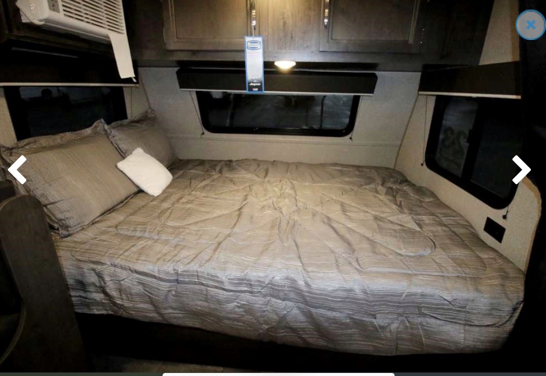 This RV rental bedroom features a bed with gray bedding, pillows, an overhead AC unit, windows, and upper cabinets.. Jayco Baja 2020