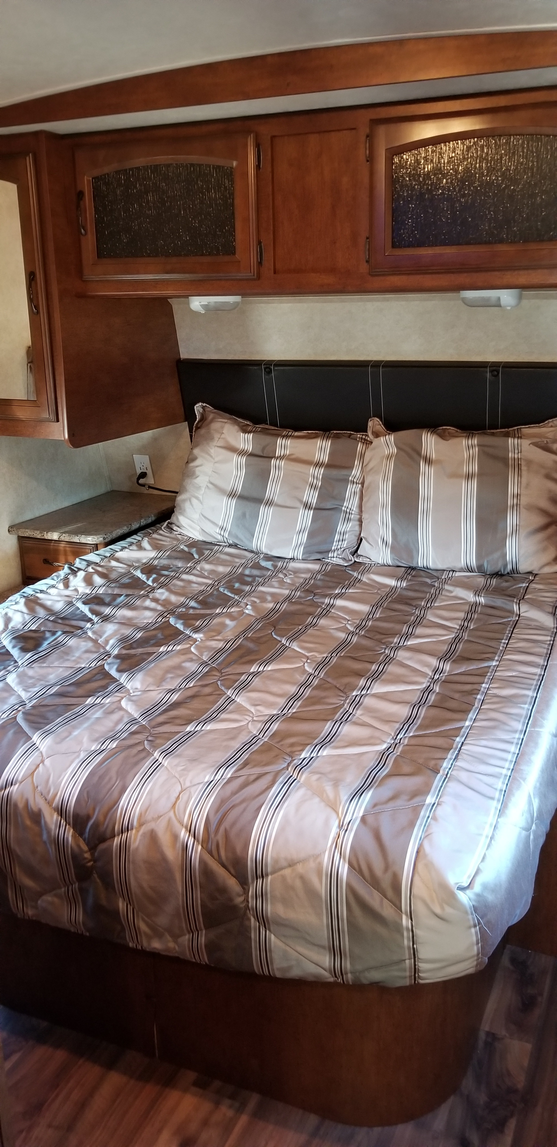 RV rental bedroom view: cozy bed with striped bedding, wood cabinets, and built-in nightstand.. Forest River Salem Hemisphere Lite 2015