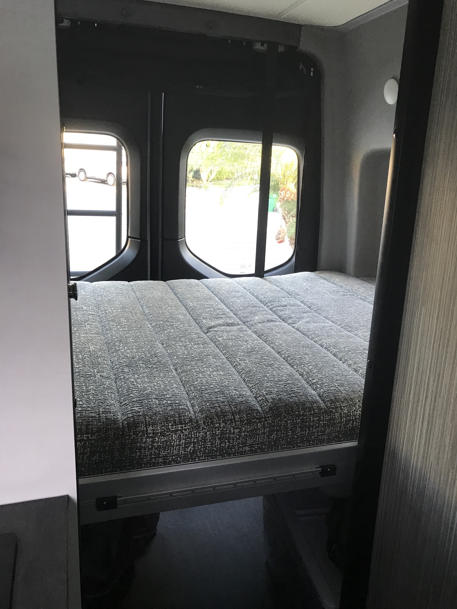 RV rental: Compact sleeping area with a grey textured bed and rear windows, inside a camper van.. Mercedes Sprinter 2020