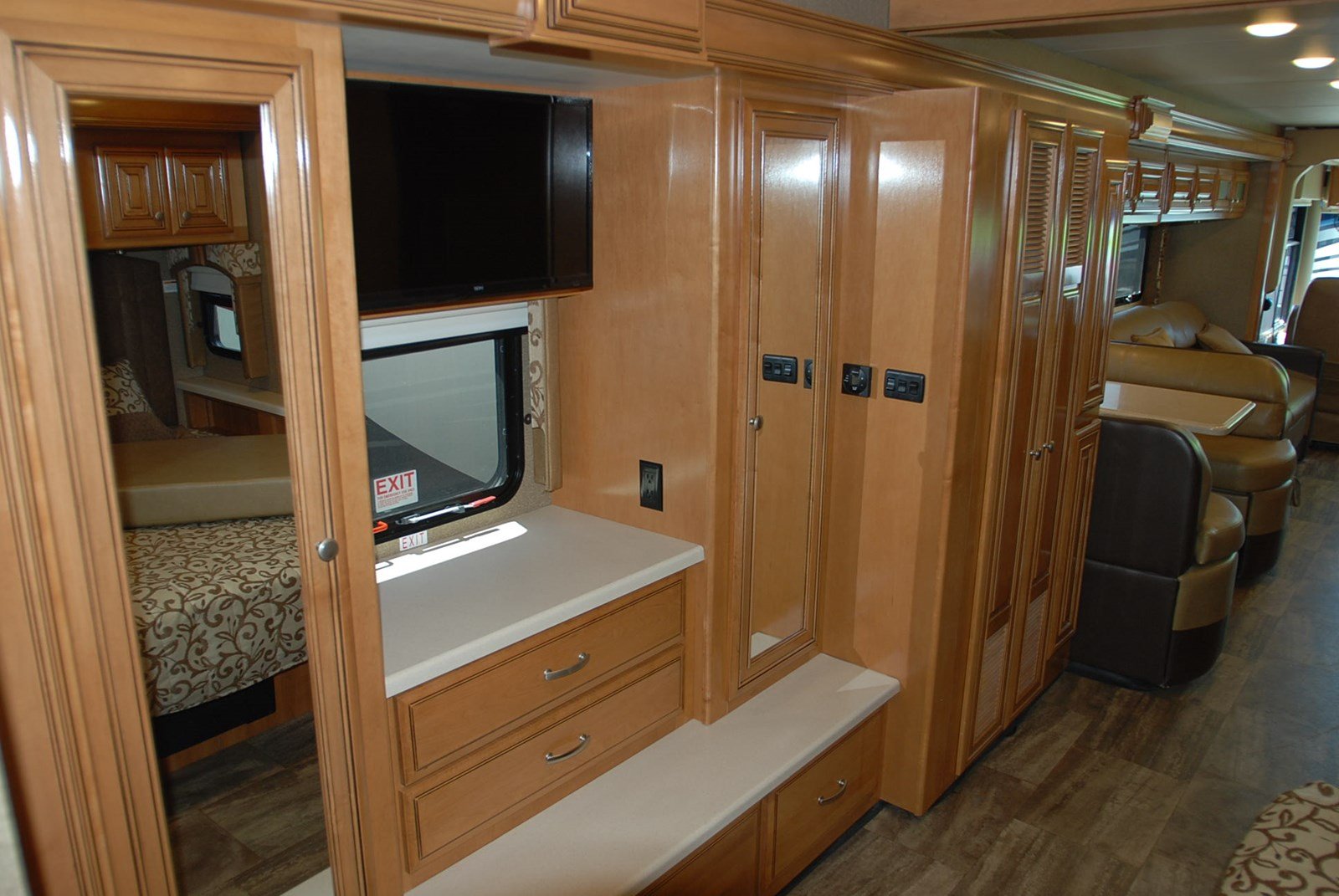 Spacious RV rental interior: light wood cabinetry, mounted TV, bed, window with exit sign, and dinette seating.. Thor Palazzo 2016