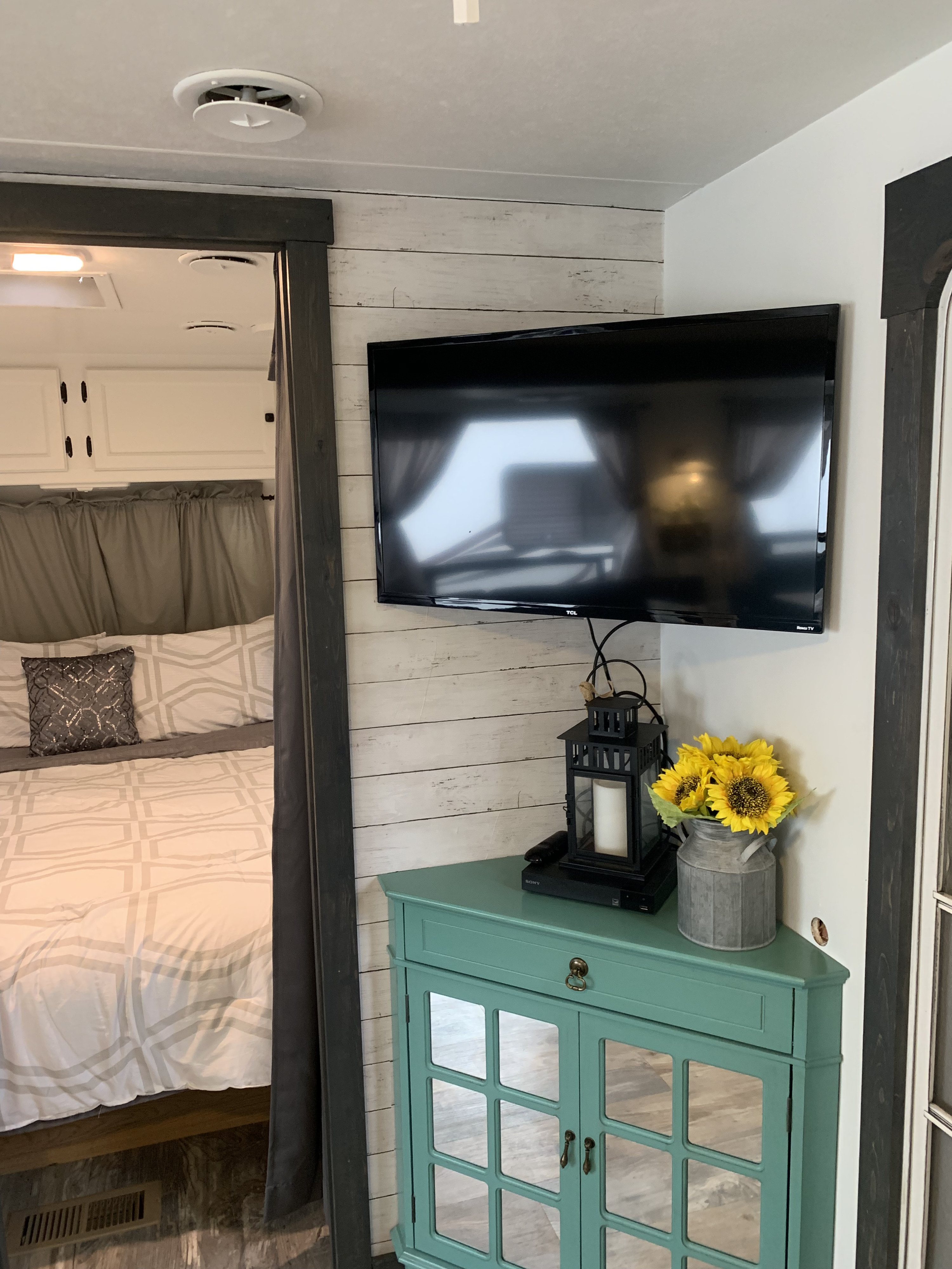 Modern RV rental interior with a cozy bedroom and living area. Features a TV mounted on a shiplap wall above a teal cabinet.. Holiday Rambler Alumascape 1999