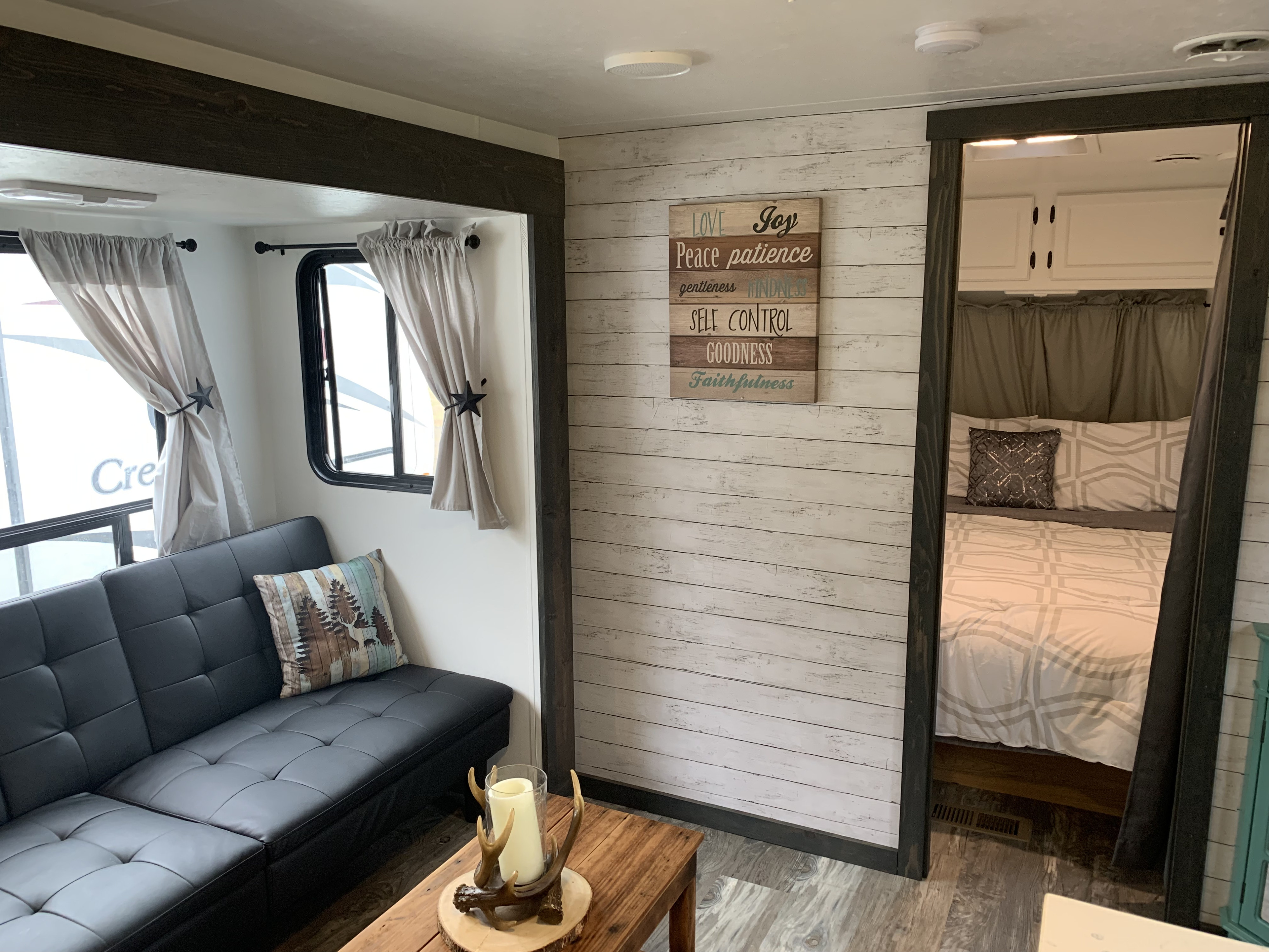 Modern RV rental interior: black sofa, rustic shiplap wall, antler decor, and a peak into the inviting bedroom.. Holiday Rambler Alumascape 1999