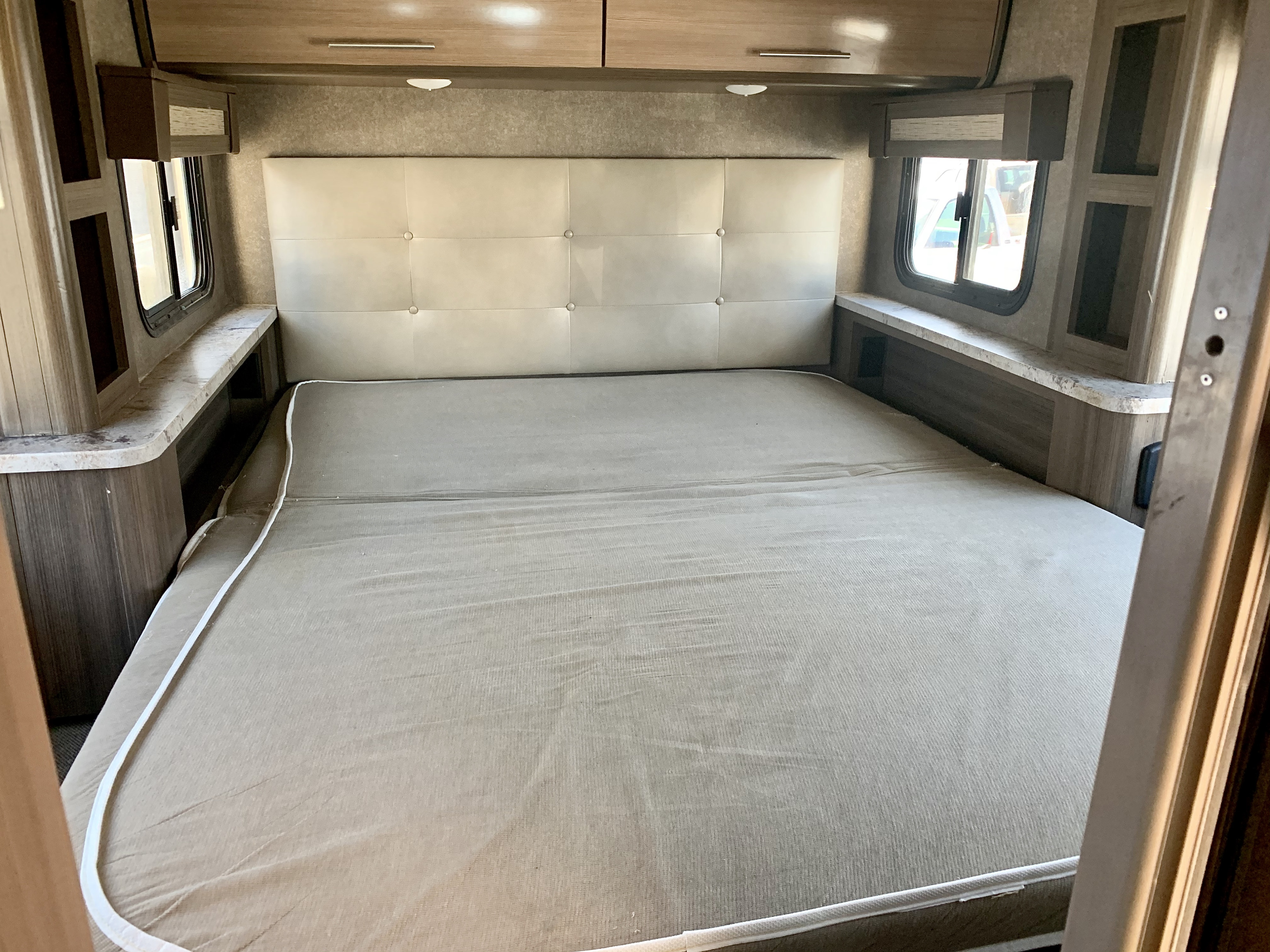 Spacious RV rental bedroom featuring a large bed with a padded headboard, side windows, and ample overhead storage.. Thor Motor Coach Compass 2018