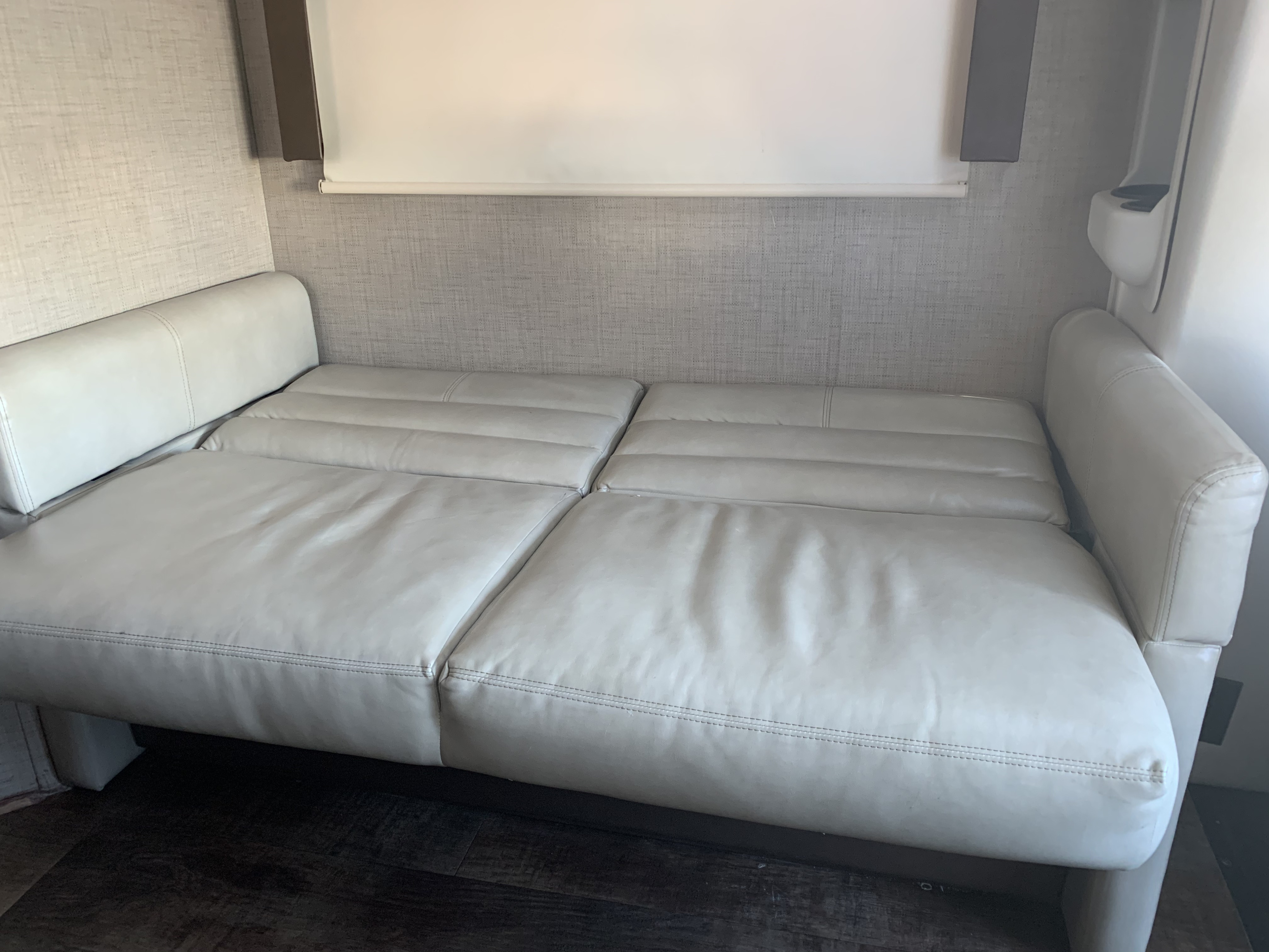 A comfortable, light-colored leatherette sofa that converts to a bed, set against a textured wall in an RV rental.. Thor Motor Coach Compass 2018