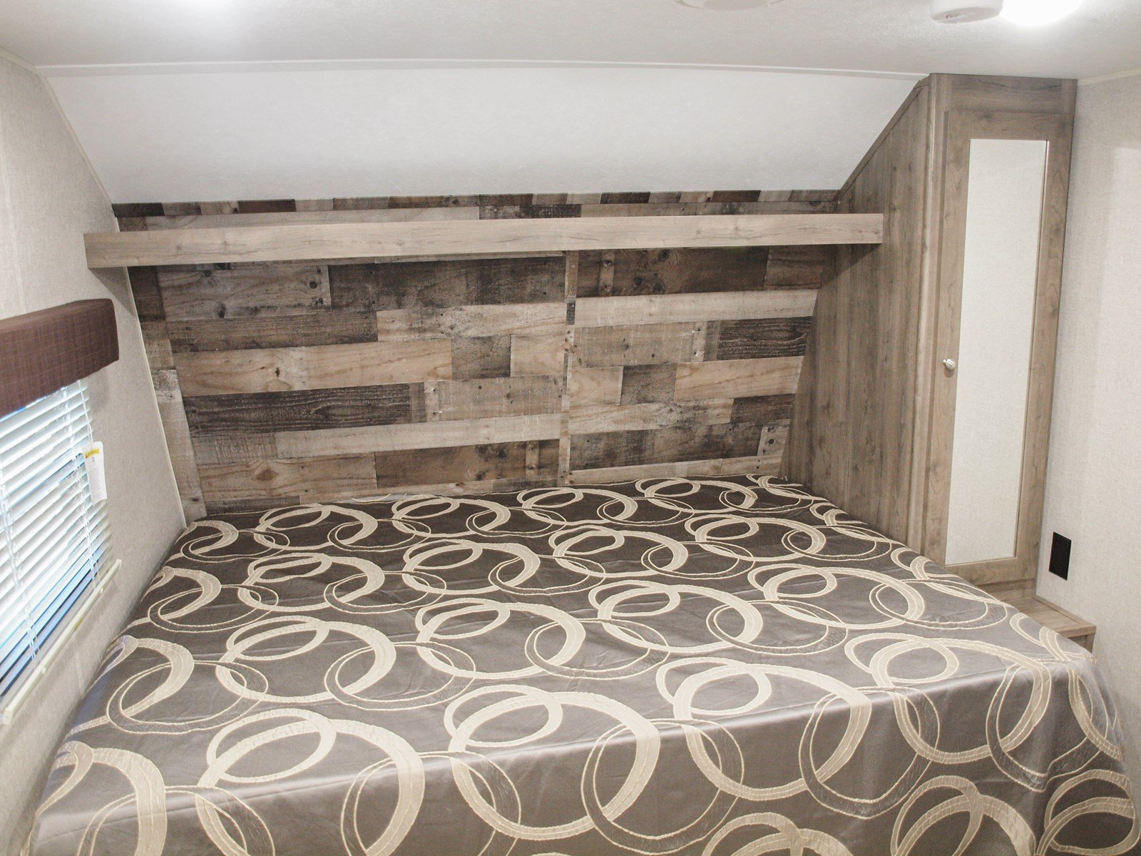 Cozy RV rental bedroom with a large bed, rustic wood headboard, window with blinds, and mirrored wardrobe, perfect for travel.. Dutchmen Aspen Trail LE 1950BH 2020