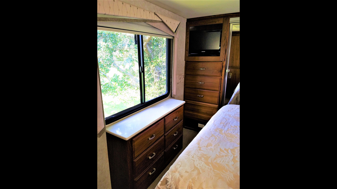 RV rental bedroom: Bright window, wood dresser, mounted TV, and bed for a comfortable journey.. Fleetwood Other 2003
