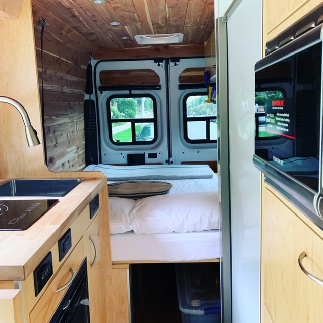 Well-appointed RV rental: kitchen with sink, induction cooktop, bed, cedar walls/ceiling, and microwave. Van life ready.. Dodge Sprinter 2500 170ext 2019