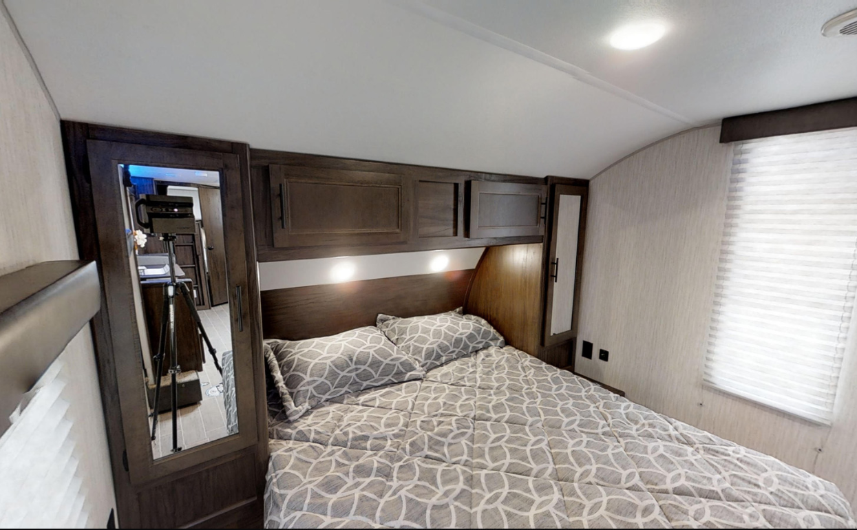 Comfortable RV rental bedroom featuring a full bed, overhead storage, and a mirror for cozy travel lodging.. Forest River Cherokee Grey Wolf 2020