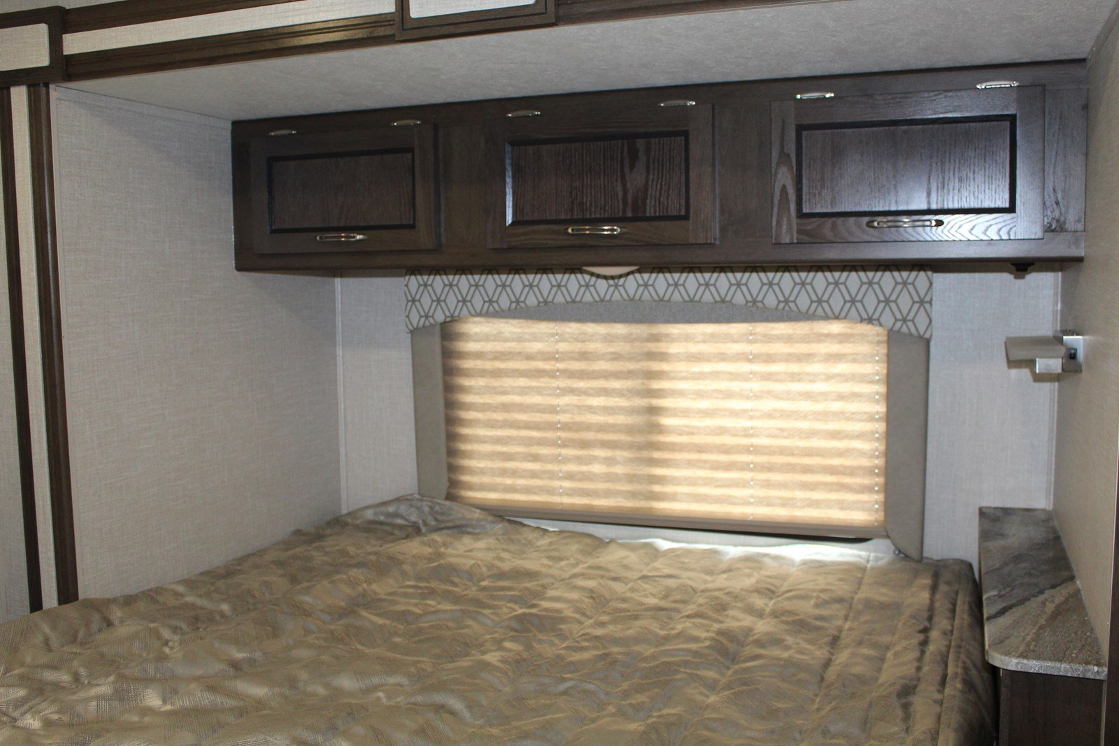 Cozy RV rental bedroom featuring a large bed, overhead storage, and a window with a pleated shade for comfortable travel.. Coachmen Freelander 2020
