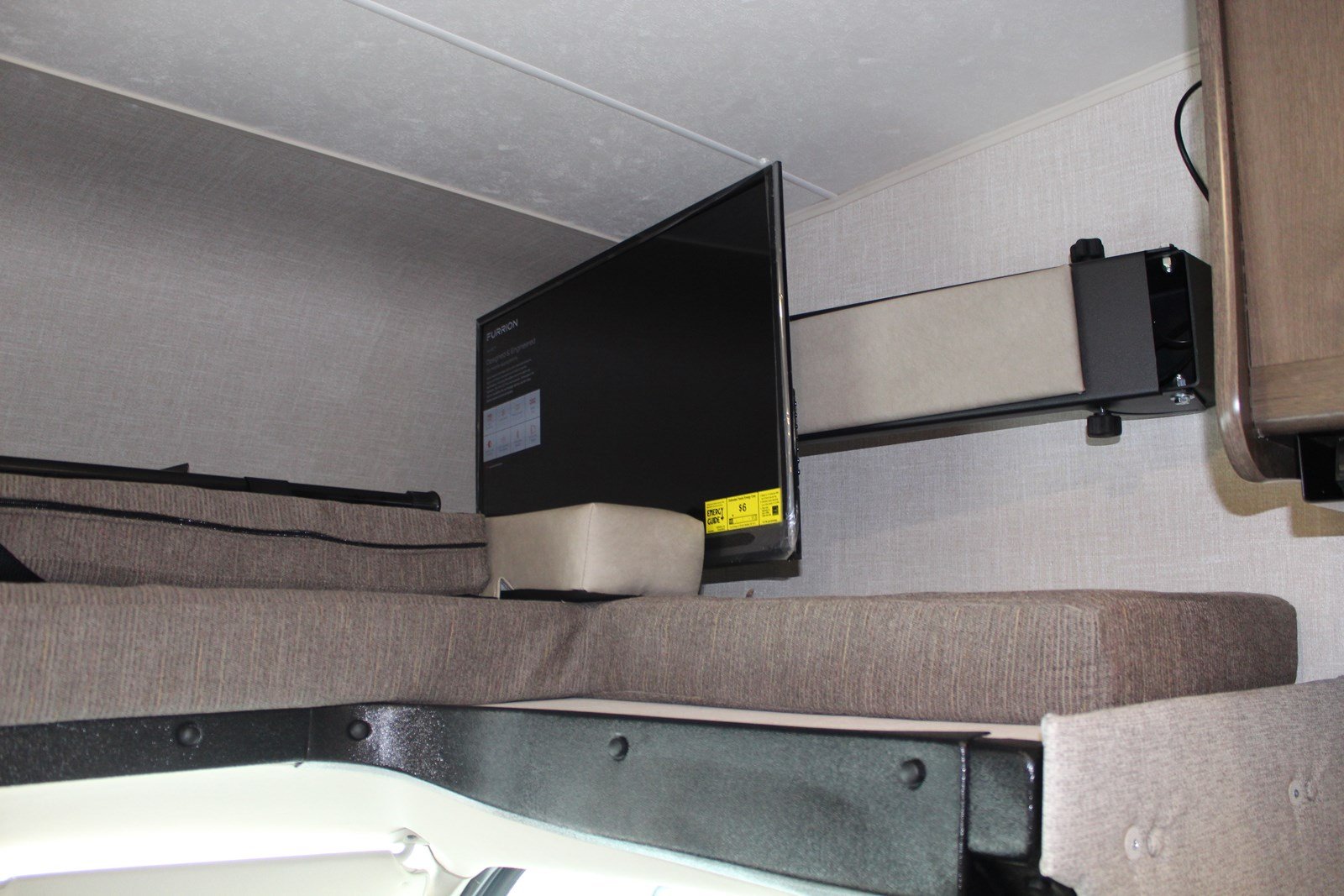 Cozy RV rental interior shows a mounted Furrion TV extended for viewing above a padded sleeping bunk.. Coachmen Freelander 2020