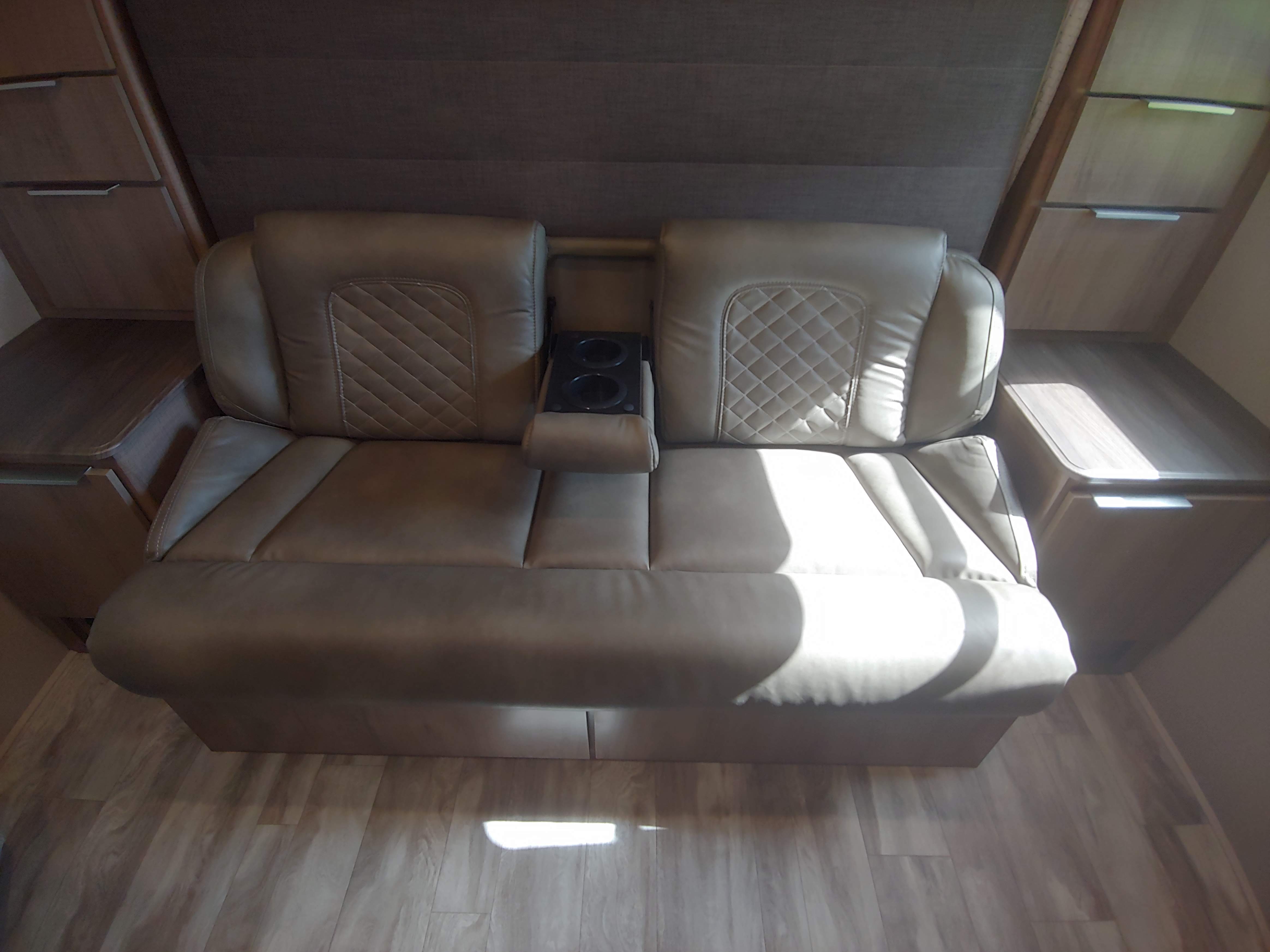 Comfortable RV rental interior featuring a tan dual recliner sofa with cup holders and adjacent storage cabinets.. Grand Design Imagine XLS 21BHE 2020