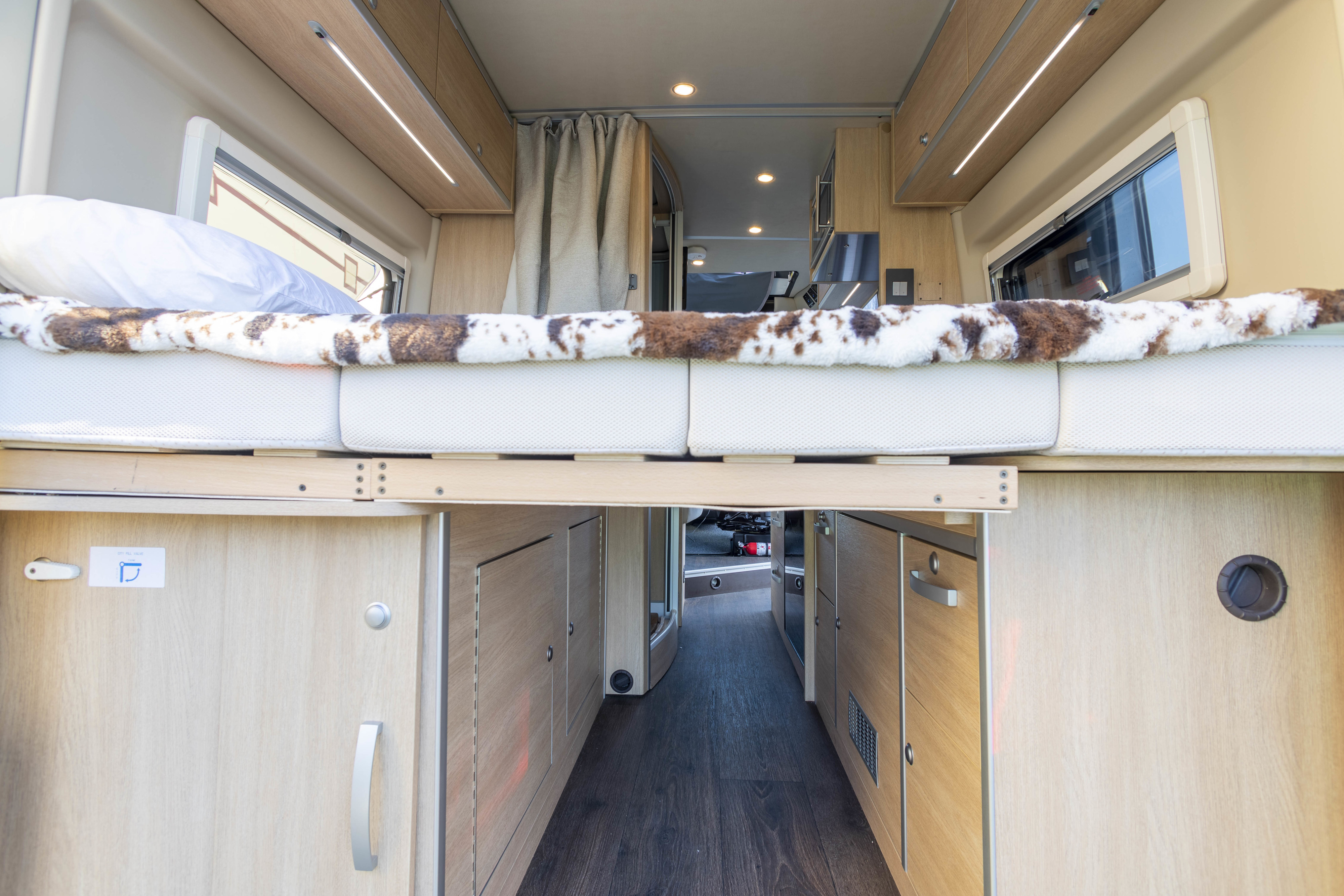 Cozy RV rental interior: A raised bed with a cow-print blanket, storage below, and an aisle leading to the camper's front.. Hymer Other 2019