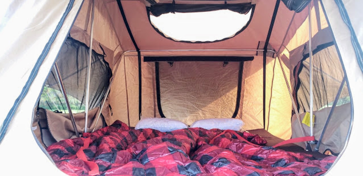 Cozy interior of an RV rental rooftop tent. Features a comfortable bed with red and black plaid bedding, metal poles, and mesh windows.. jeep unlimited sahara 2016