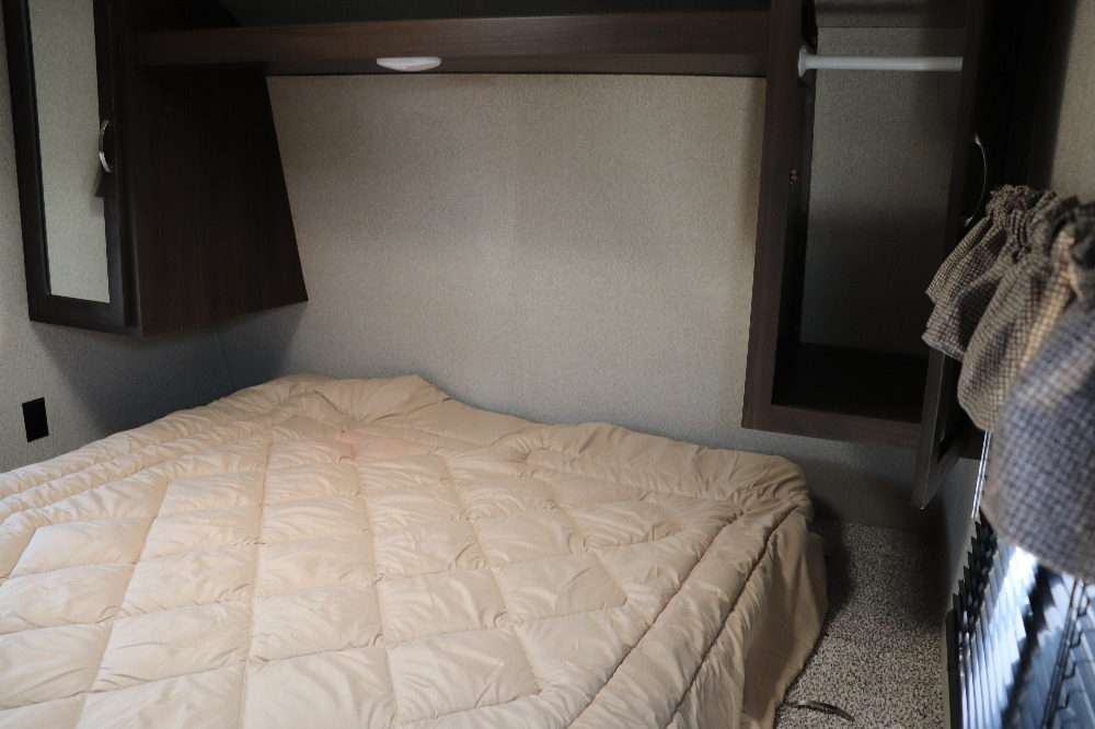 Cozy RV rental bedroom features a comfortable bed, overhead cabinets, and a wardrobe, optimizing travel space.. Keystone Springdale 2020