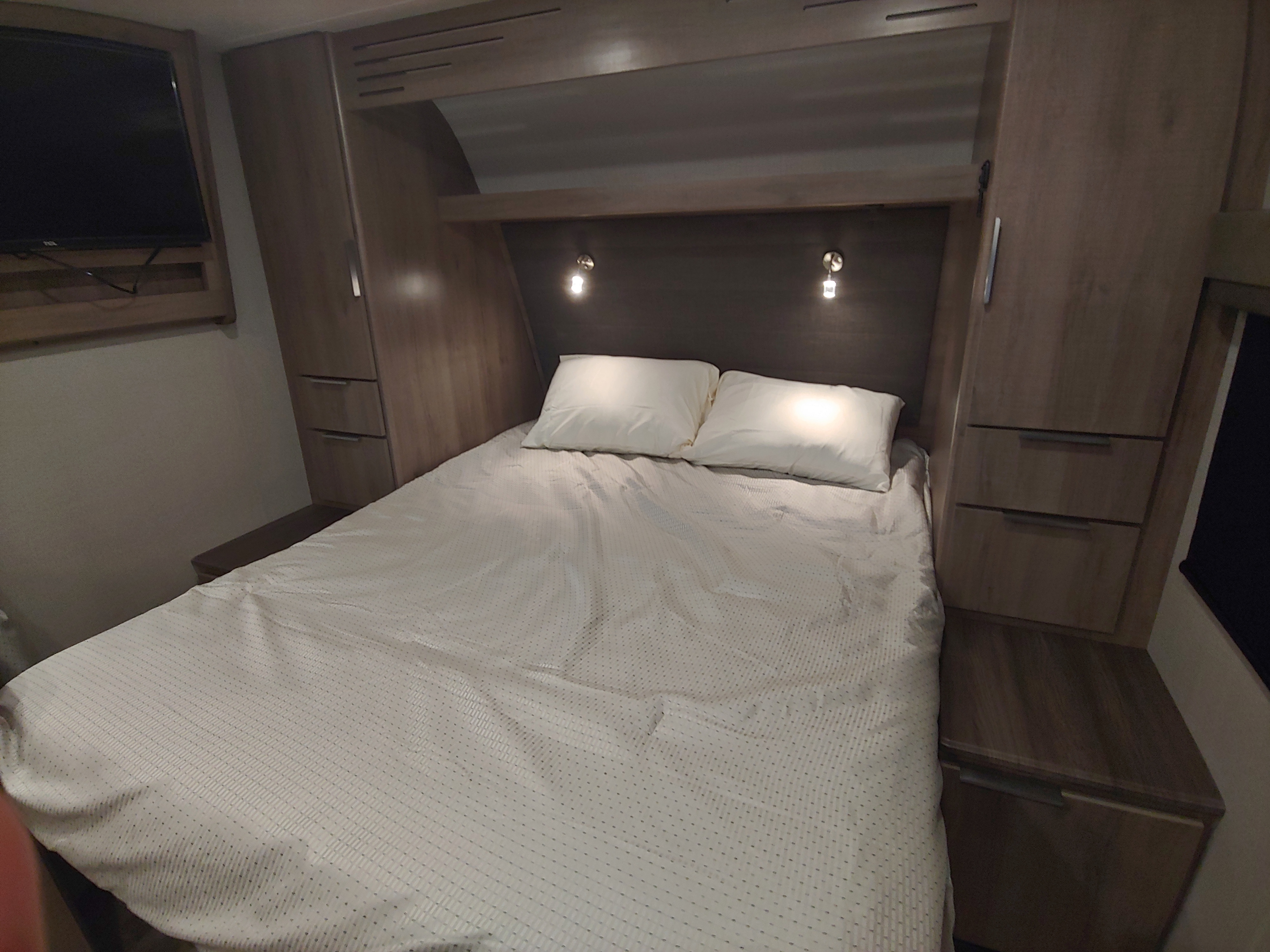 Cozy RV rental bedroom featuring a comfortable bed, built-in storage, and a TV, perfect for a relaxing getaway.. Grand Design Imagine XLS 21BHE 2020