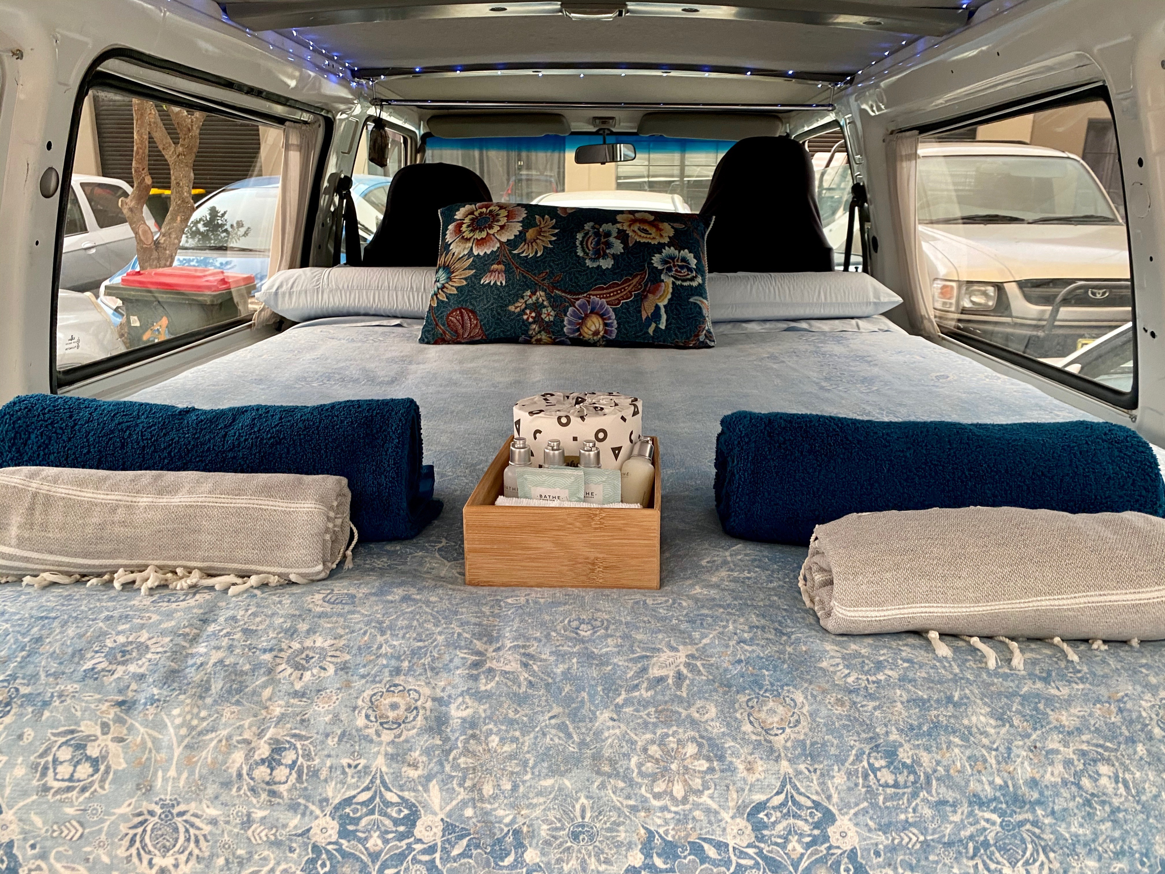 Comfortable RV rental interior with a cozy bed, soft linens, and complimentary toiletries, perfect for a relaxing road trip.. Mitsubishi Express 2003