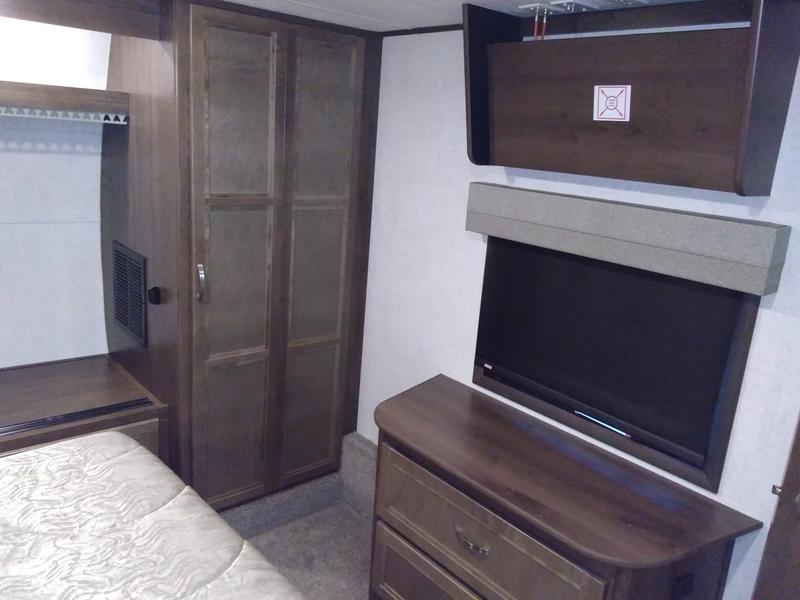Cozy RV rental bedroom featuring a bed, wood-toned wardrobe, wall-mounted TV, and dresser for storage.. Highland Ridge Mesa Ridge 427BHS 2019