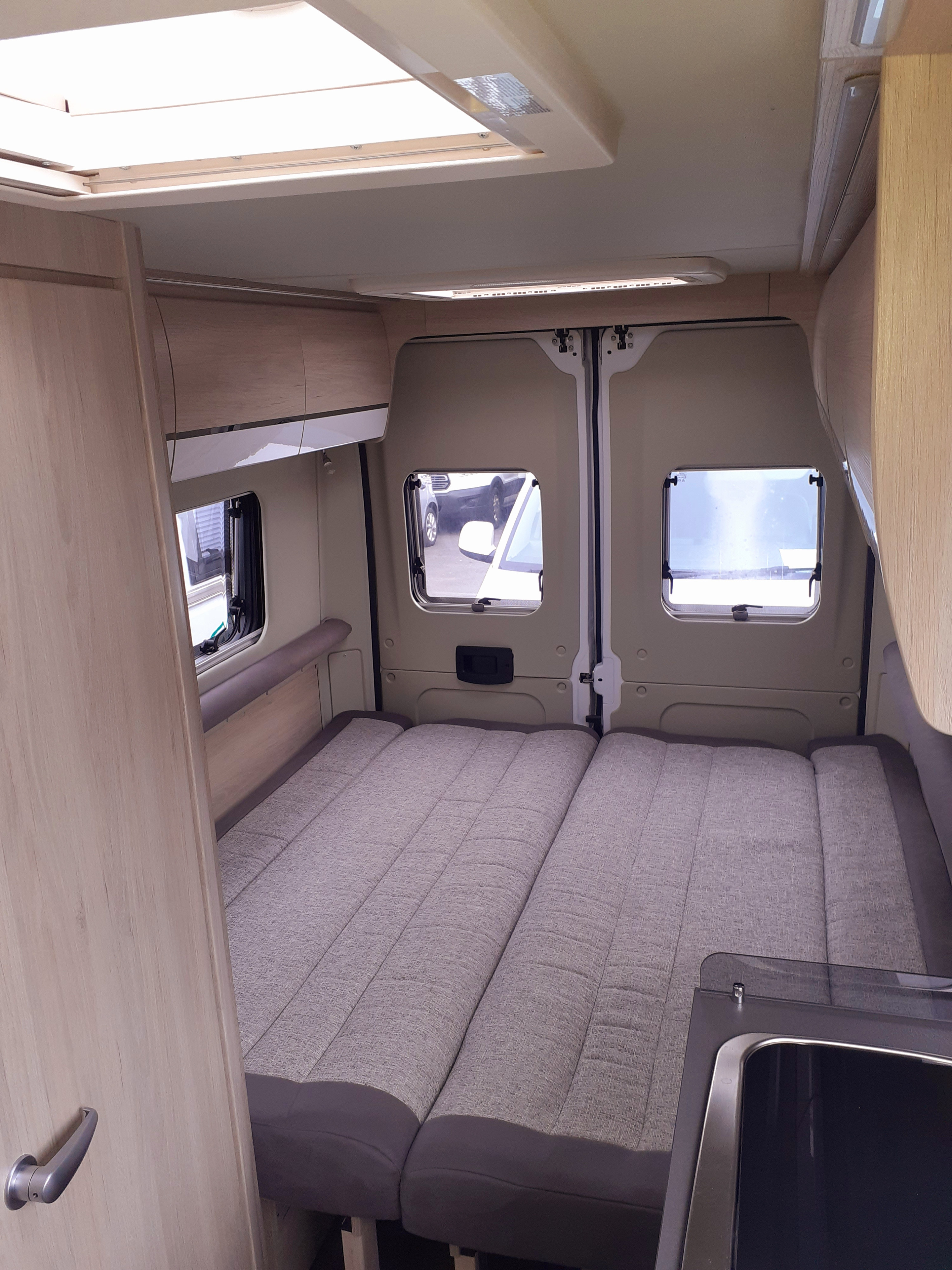 Experience the cozy interior of this RV rental, featuring a comfortable bed, windows, and a compact kitchen for your adventures.. fiat 66 2024