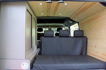 RV rental camper van interior: wood-paneled roof/walls, gray seating/bed, & storage cabinetry.. Dodge Promaster 2018
