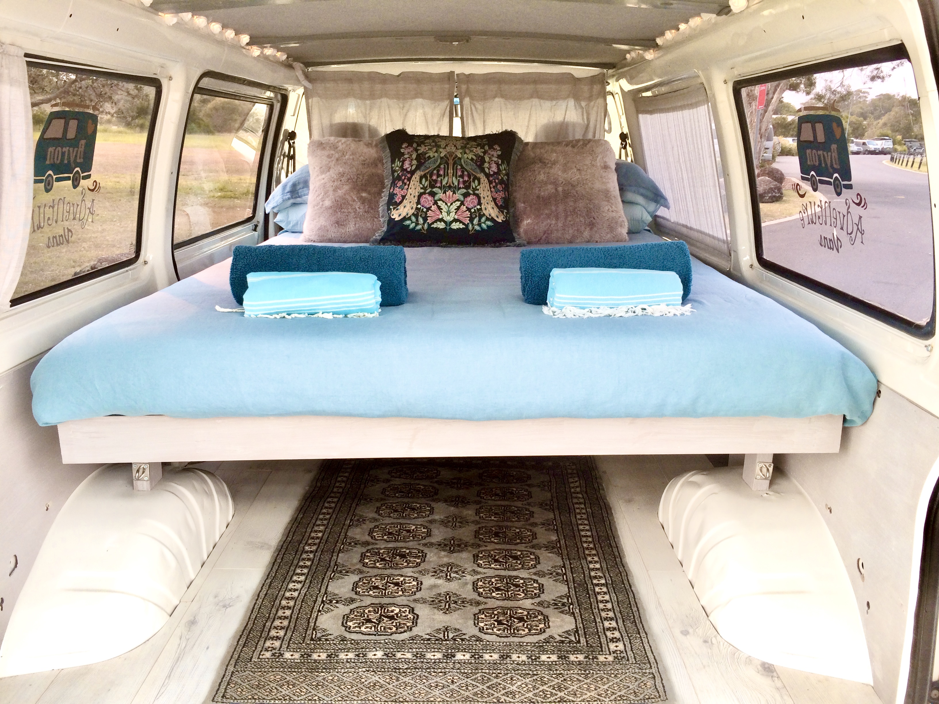 Spacious RV rental interior with a light blue bed, decorative pillows, and a classic rug. Ready for adventure.. Mitsubishi Express 2001