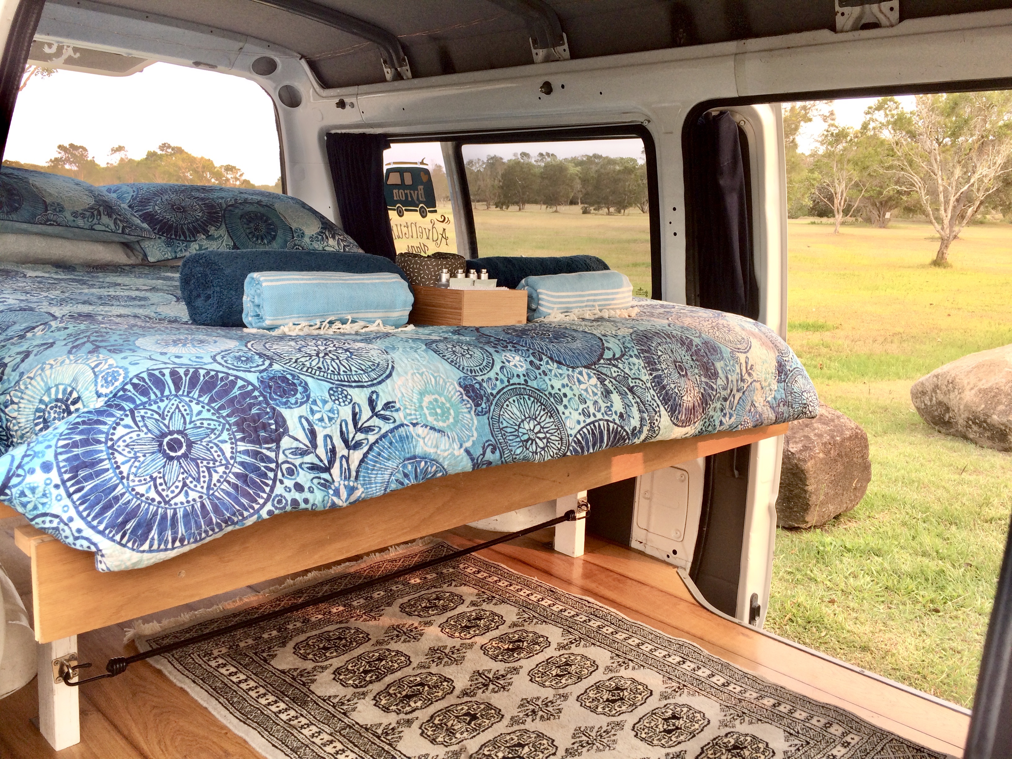 Comfortable rv rental interior: blue patterned bed, towels, and a tranquil view of nature. Your adventure awaits!. Mitsubishi Express SJ 1999