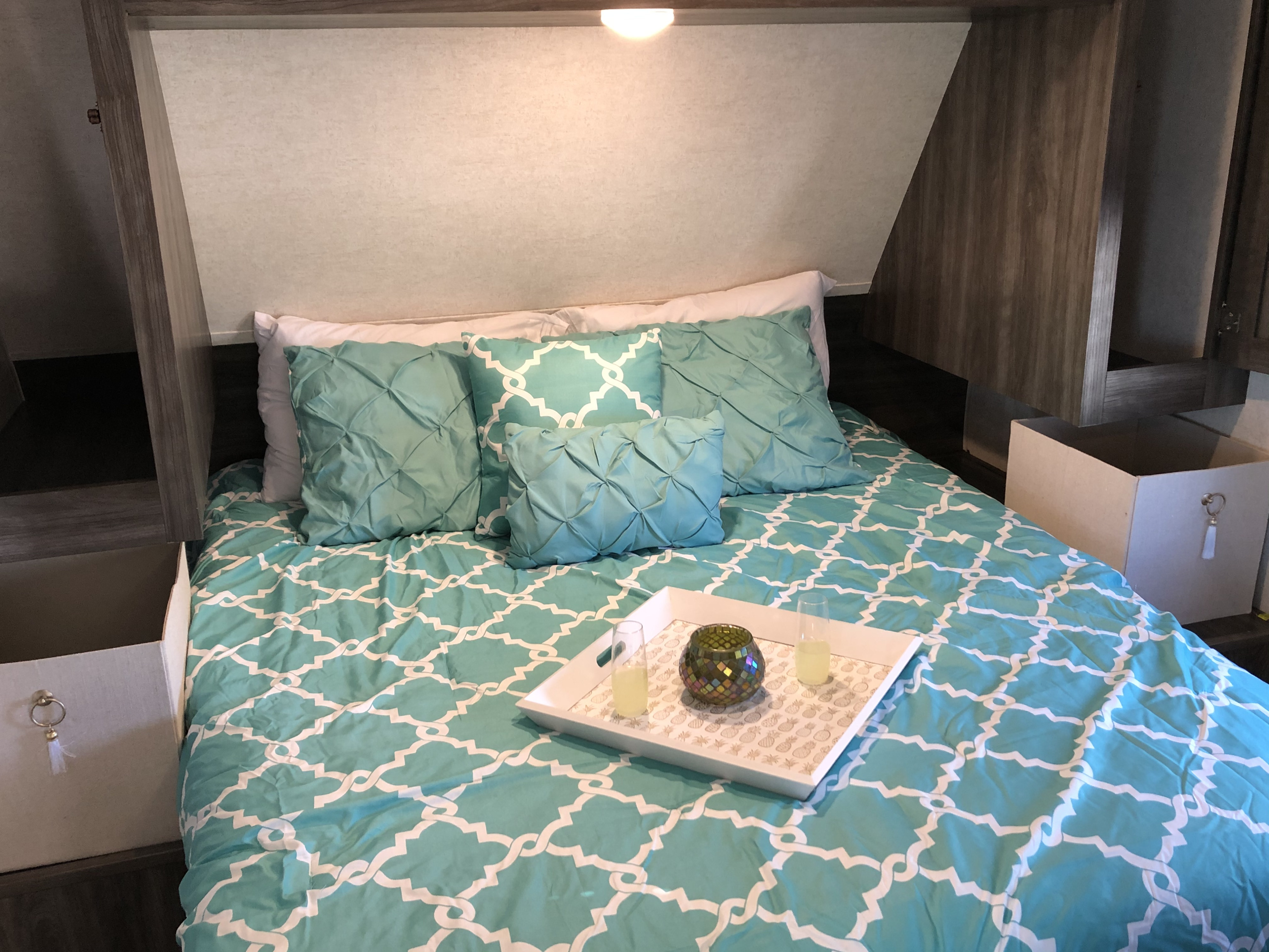Cozy RV rental bedroom with queen bed, turquoise bedding, accent pillows, and practical built-in storage.. Highland Ridge RV Open Range 2019