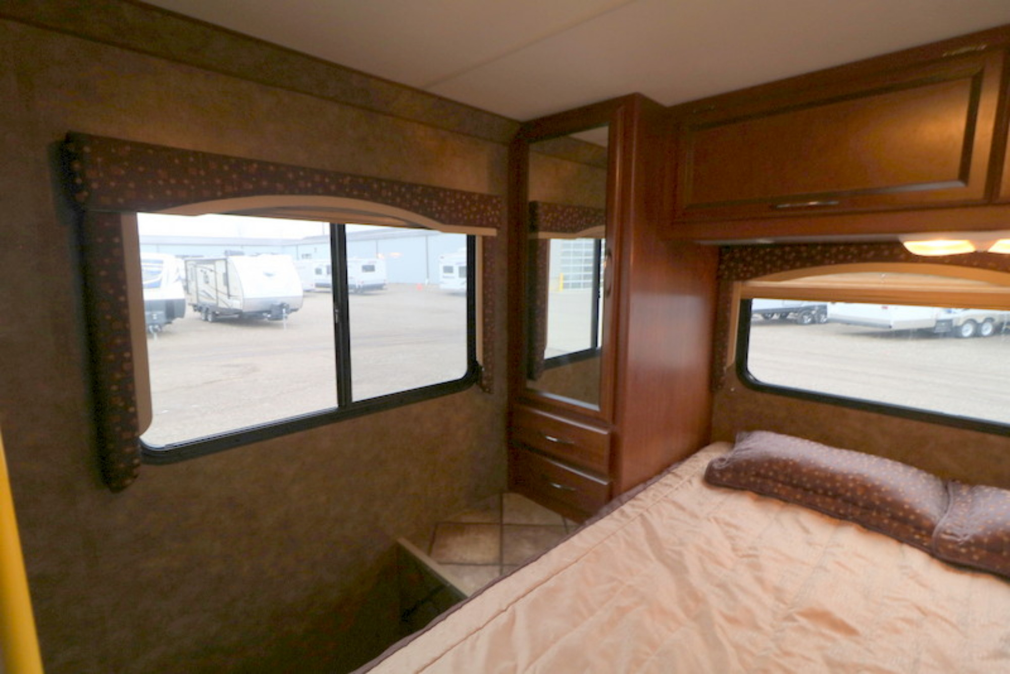 This RV rental bedroom features a bed, windows showing other RVs outside, a mirrored wardrobe, and overhead cabinets.. Thor Motor Coach Freedom Elite 2013
