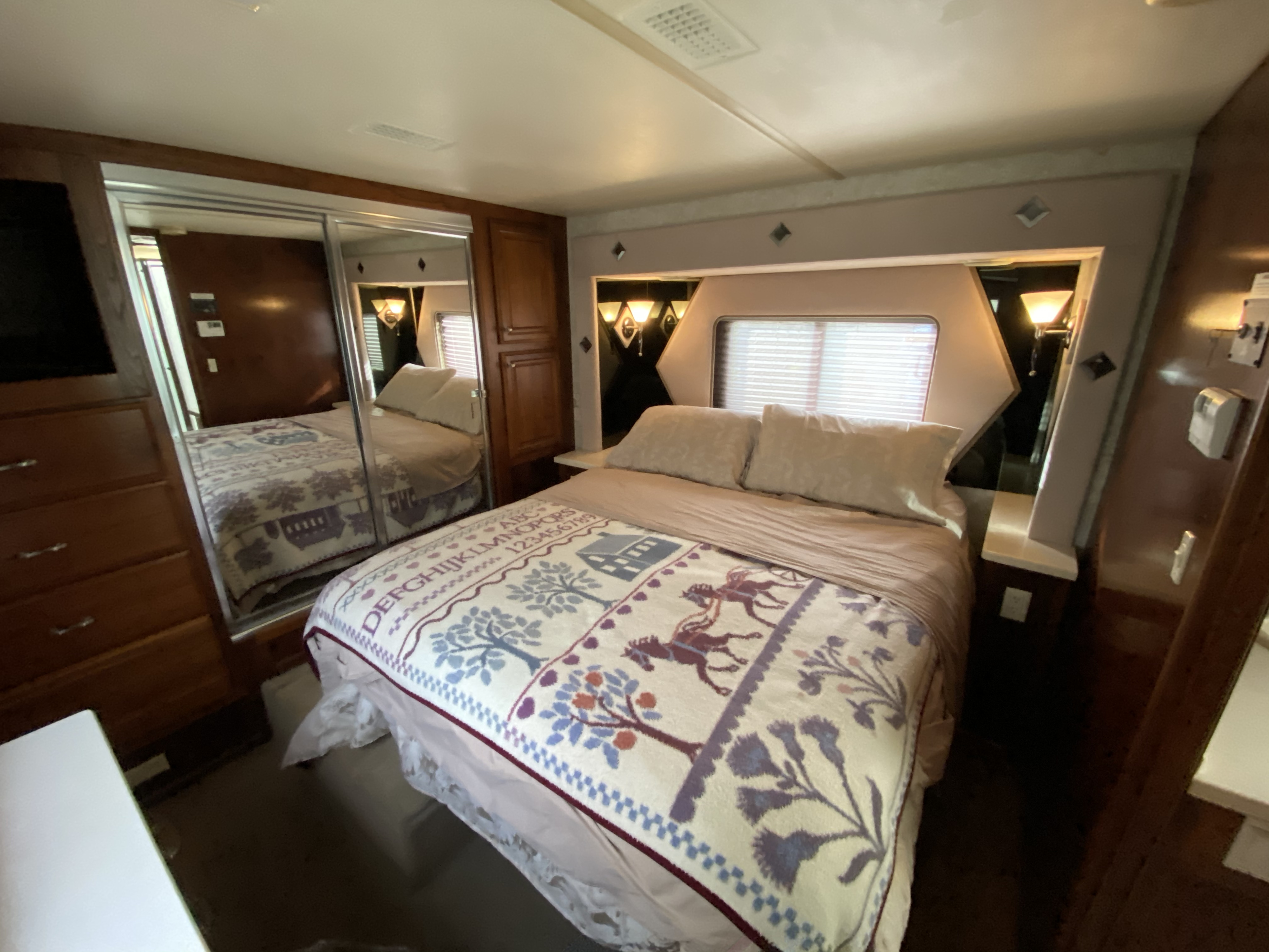 Cozy RV rental bedroom with a comfortable bed, mirrored closet, built-in lighting, and warm wood tones. Ideal for travel.. Fleetwood Other 2003