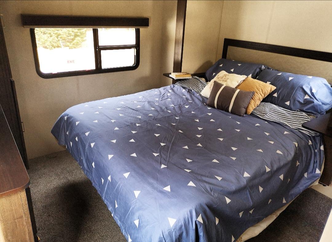 Cozy RV rental bedroom features a queen bed with blue triangle-patterned bedding, accent pillows, and an exit window.. Forest River Salem Hemisphere GLX 2018