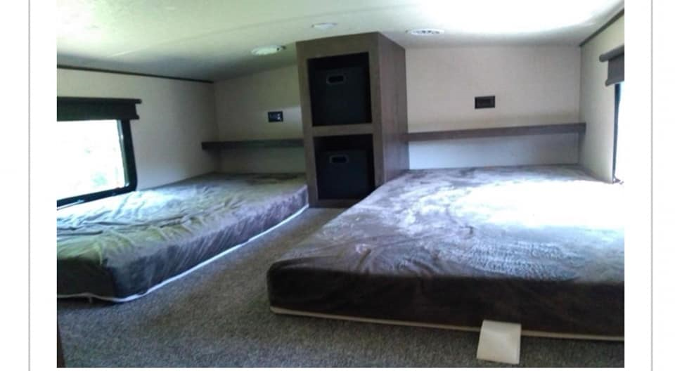 Inside an RV rental bunk room with two low beds, a central storage unit, and windows for light. Sleep comfortably on the road.. Forest River Salem Hemisphere GLX 2018