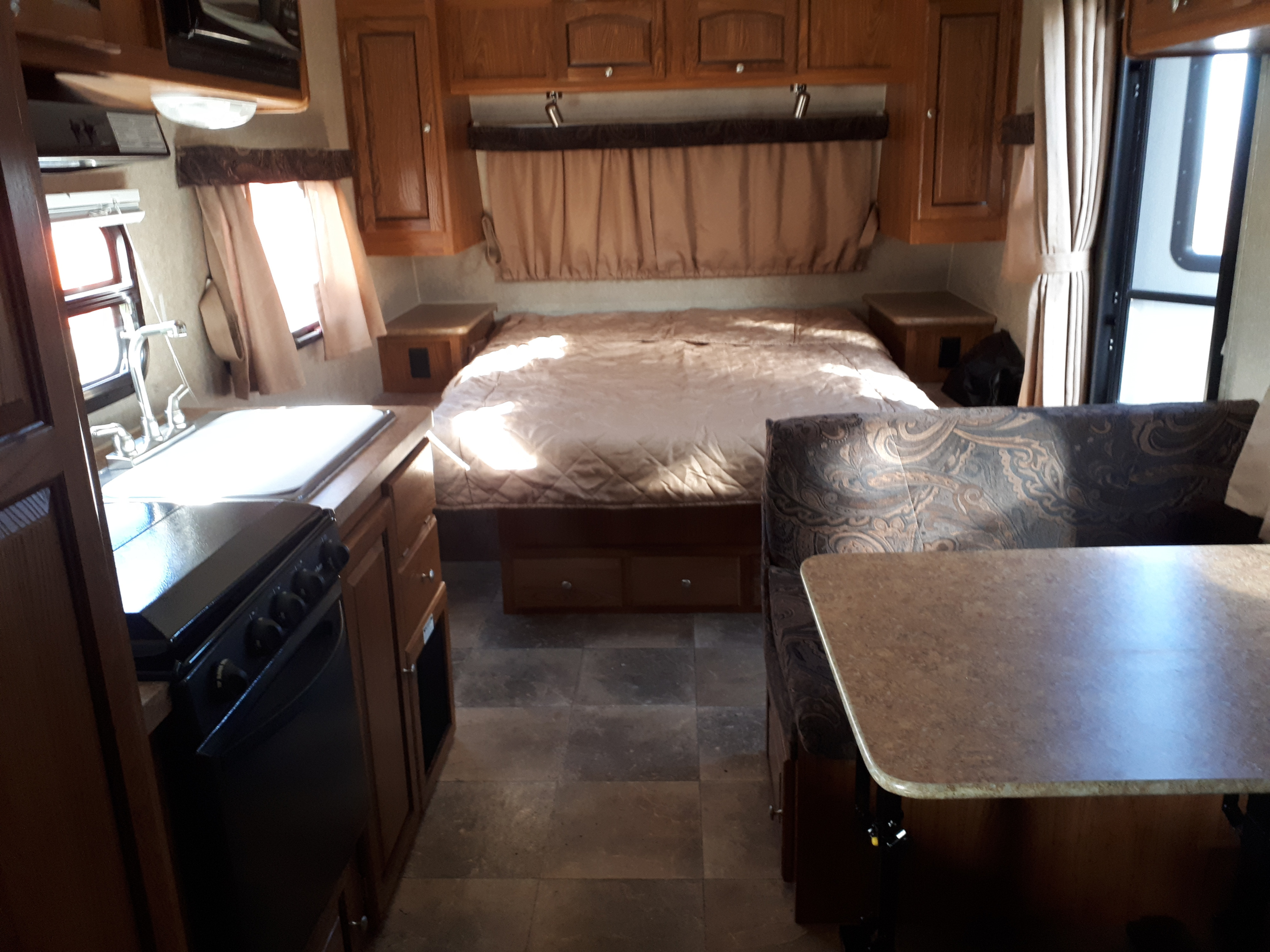 Comfortable rv rental interior featuring a cozy bed, well-equipped kitchenette with sink and stove, and a dinette.. Forest River Rockwood Mini Lite 2012