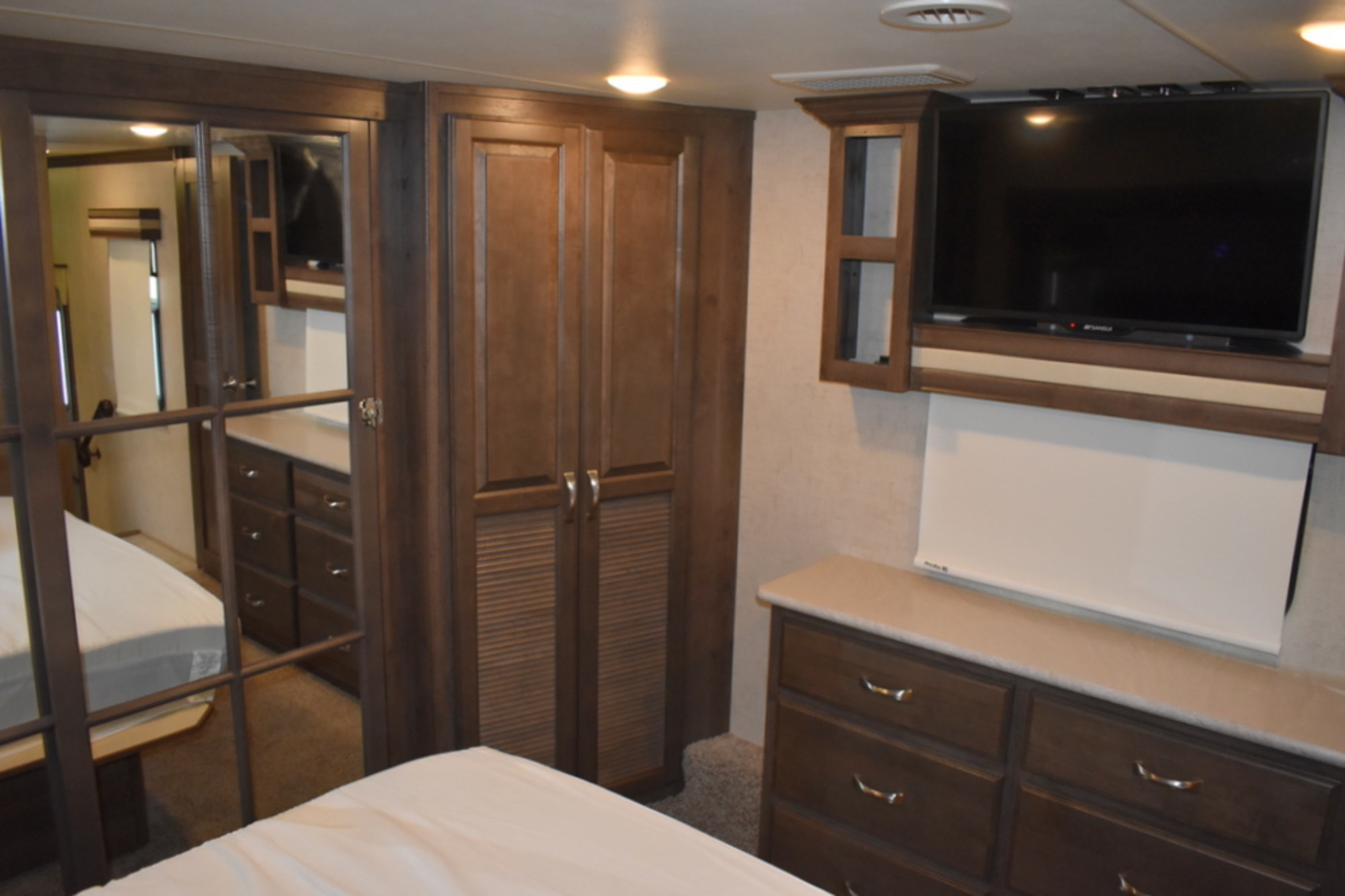 RV rental bedroom with sleek wooden cabinets, mirrored closet, dresser, and wall-mounted TV for a comfortable stay.. K-Z Manufacturing Venom 2017