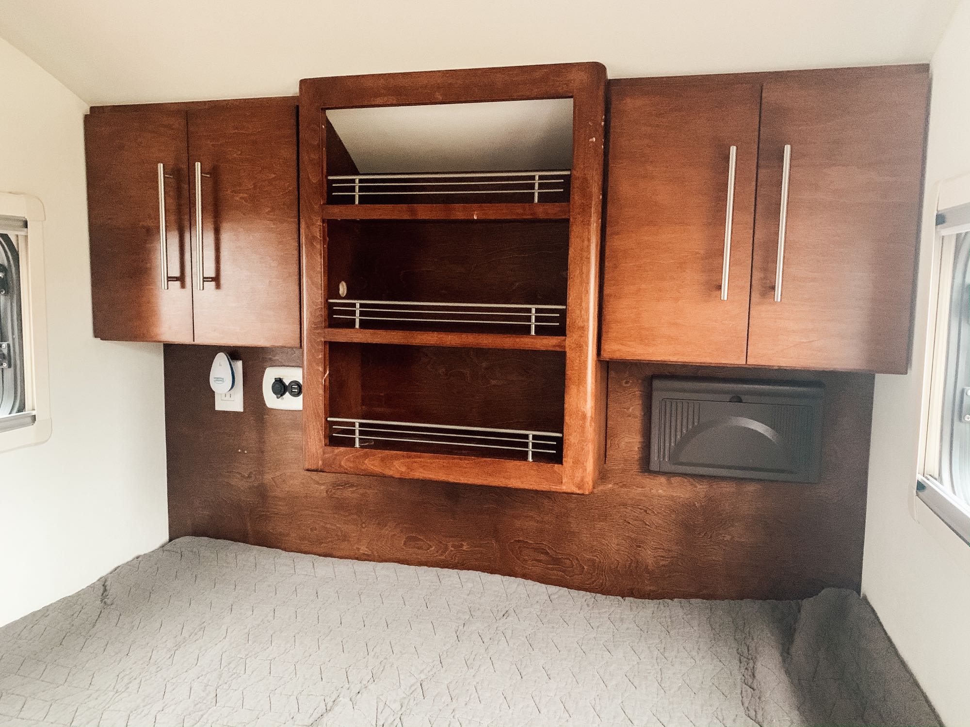 RV rental interior: cozy bedroom with dark wood cabinets, central open shelving, and a grey quilted bed. Functional small space.. T@G T@G Trailer 2016