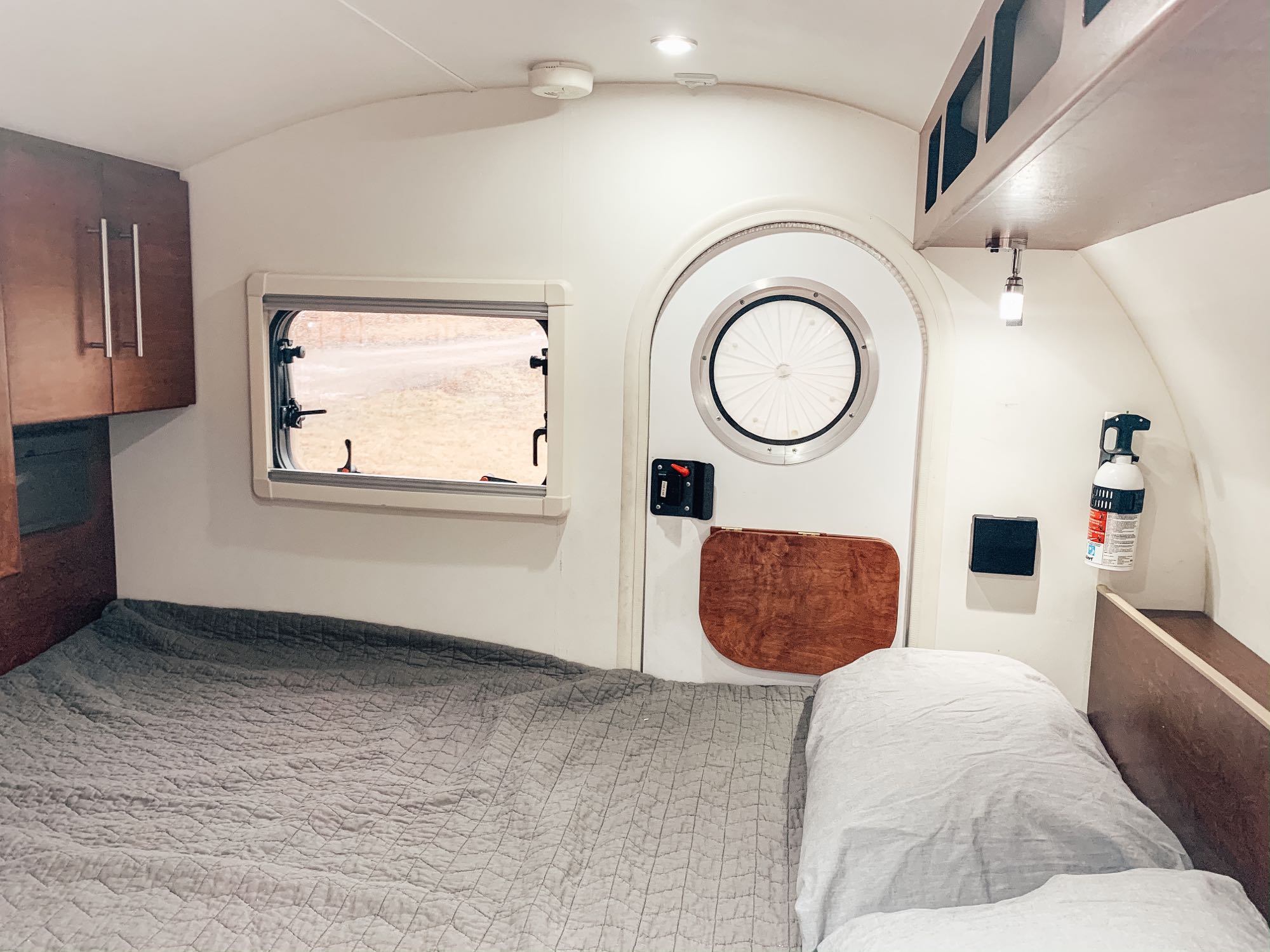 Interior of a compact RV rental bedroom, featuring a large bed, wooden cabinets, and a distinctive round entry door.. T@G T@G Trailer 2016