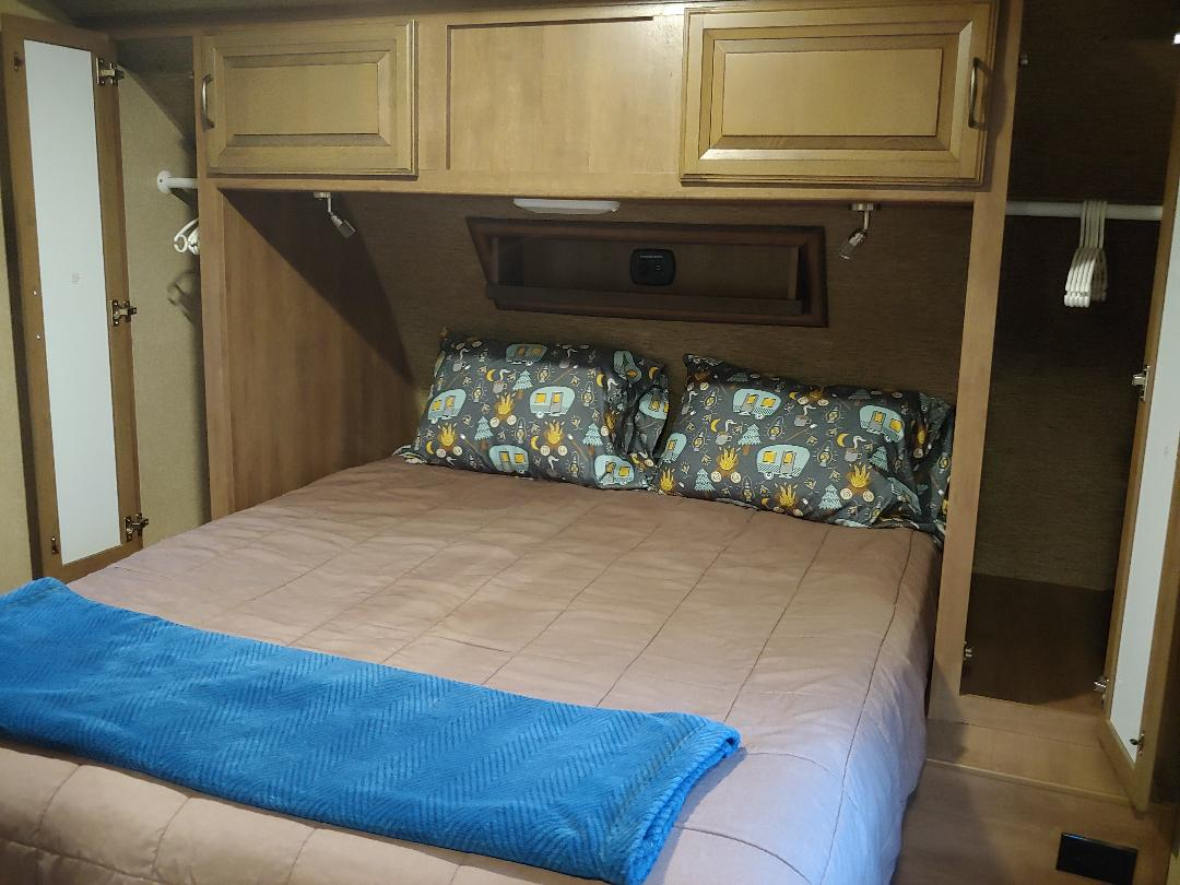 Interior of an RV rental bedroom with a bed, patterned pillows, blue blanket, and integrated cabinets.. Cruiser Rv Corp Fun Finder 2017