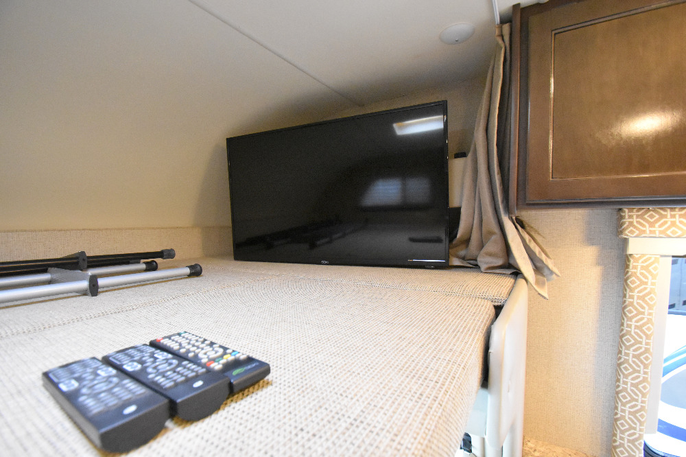 RV rental: Overhead bed with TV, remotes, and support poles visible, offering a functional and cozy interior space.. Thor Motor Coach Freedom Elite 2017