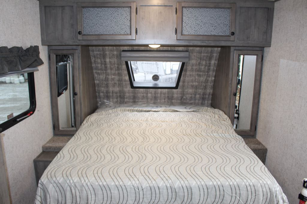 Cozy RV rental bedroom featuring a bed with wavy patterned duvet, overhead cabinets, and mirrored side storage.. Coachmen Apex 208BHS 2023
