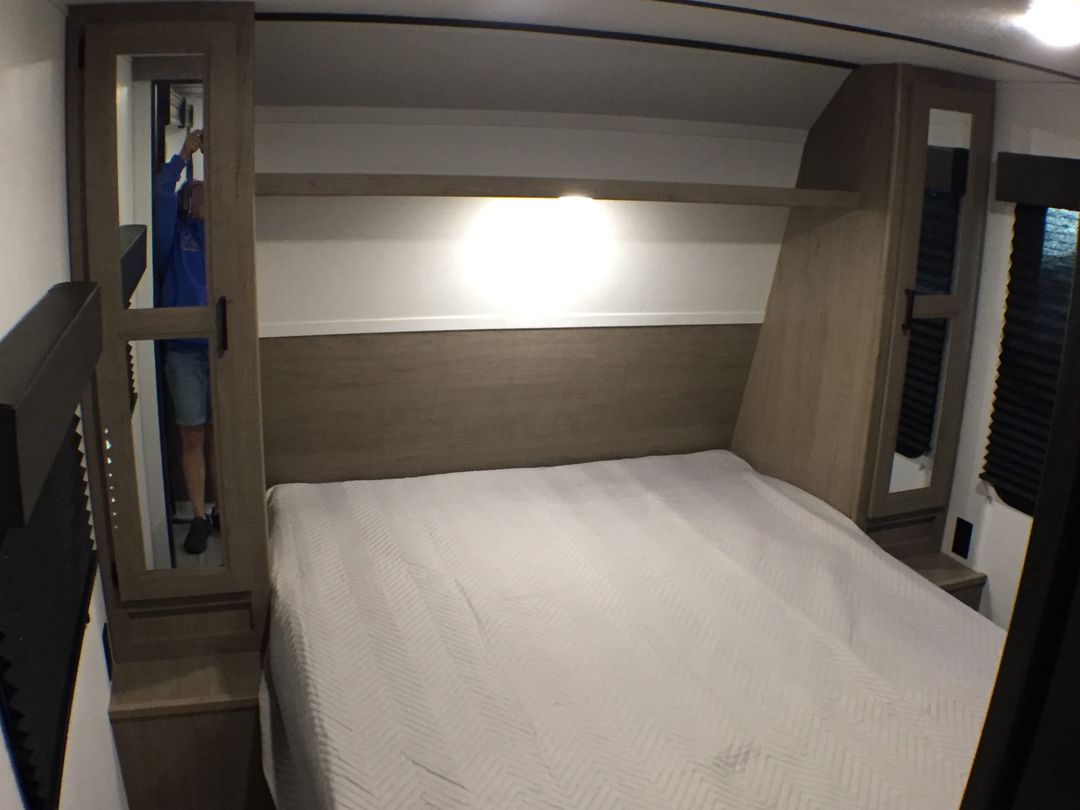 Inside an RV rental: a cozy bedroom with a comfortable bed, overhead shelf, and mirrored storage cabinets.. Keystone Hideout 2020