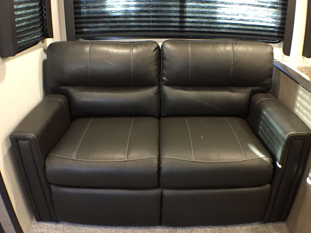 Comfortable dark gray two-seat RV recliner sofa with white stitching, ready for your next RV rental.. Keystone Hideout 2020