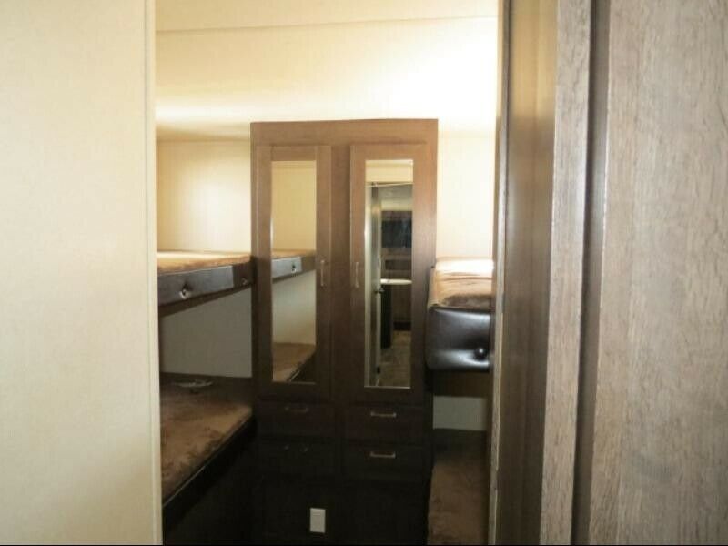 RV rental interior with multiple brown-cushioned bunk beds & central mirrored wardrobe. Offers sleeping & storage for travel.. Forest River Wildwood X-Lite 2019
