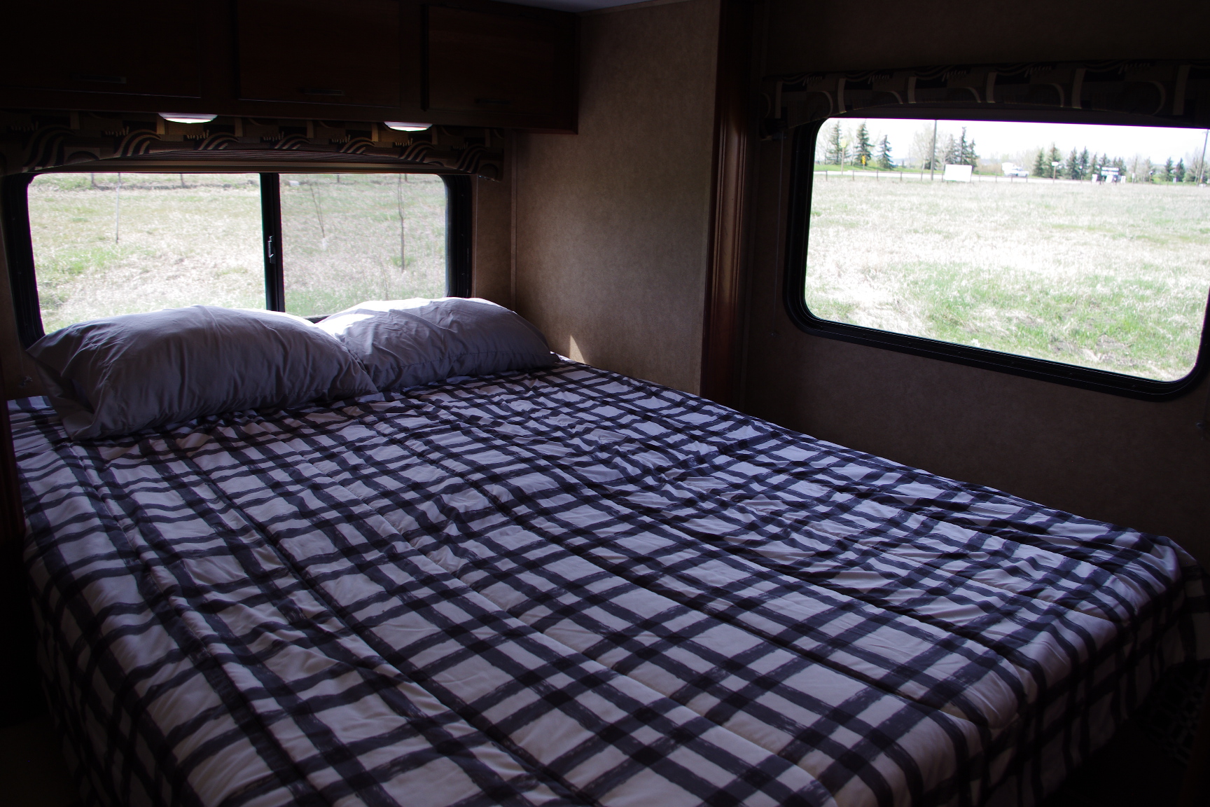 Comfortable RV rental bedroom featuring a plaid bed, pillows, and scenic field views through windows. Ideal for travel.. Forest River Sunseeker 2015