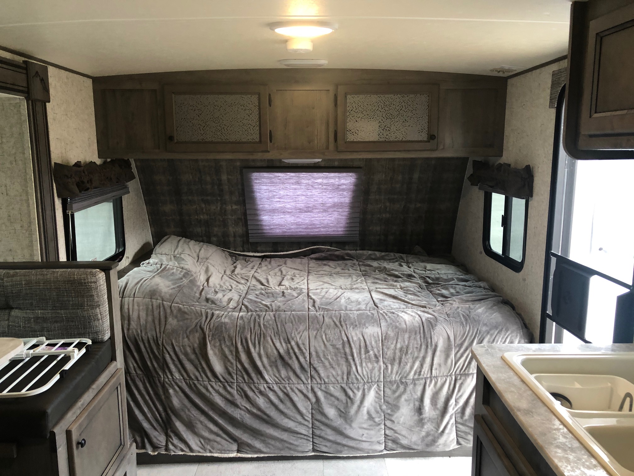Cozy RV rental bedroom with a large bed, overhead cabinets, and a glimpse of the kitchen sink, ready for travel.. Coachmen Apex Nano 2019