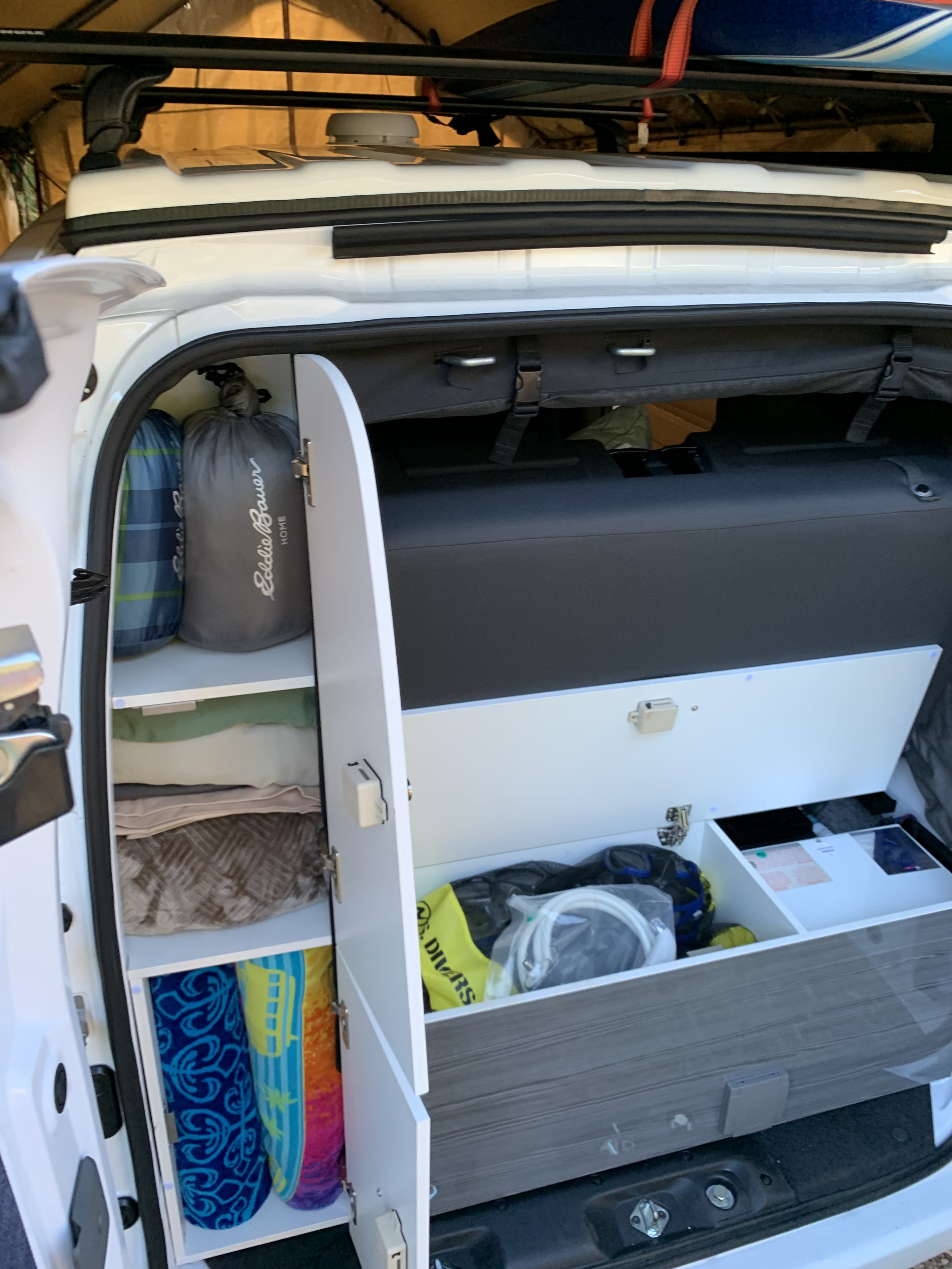 Organized RV rental: A look inside a camper van's custom storage with sleeping bags, blankets, towels, and road trip gear.. Nissan NV200 2019