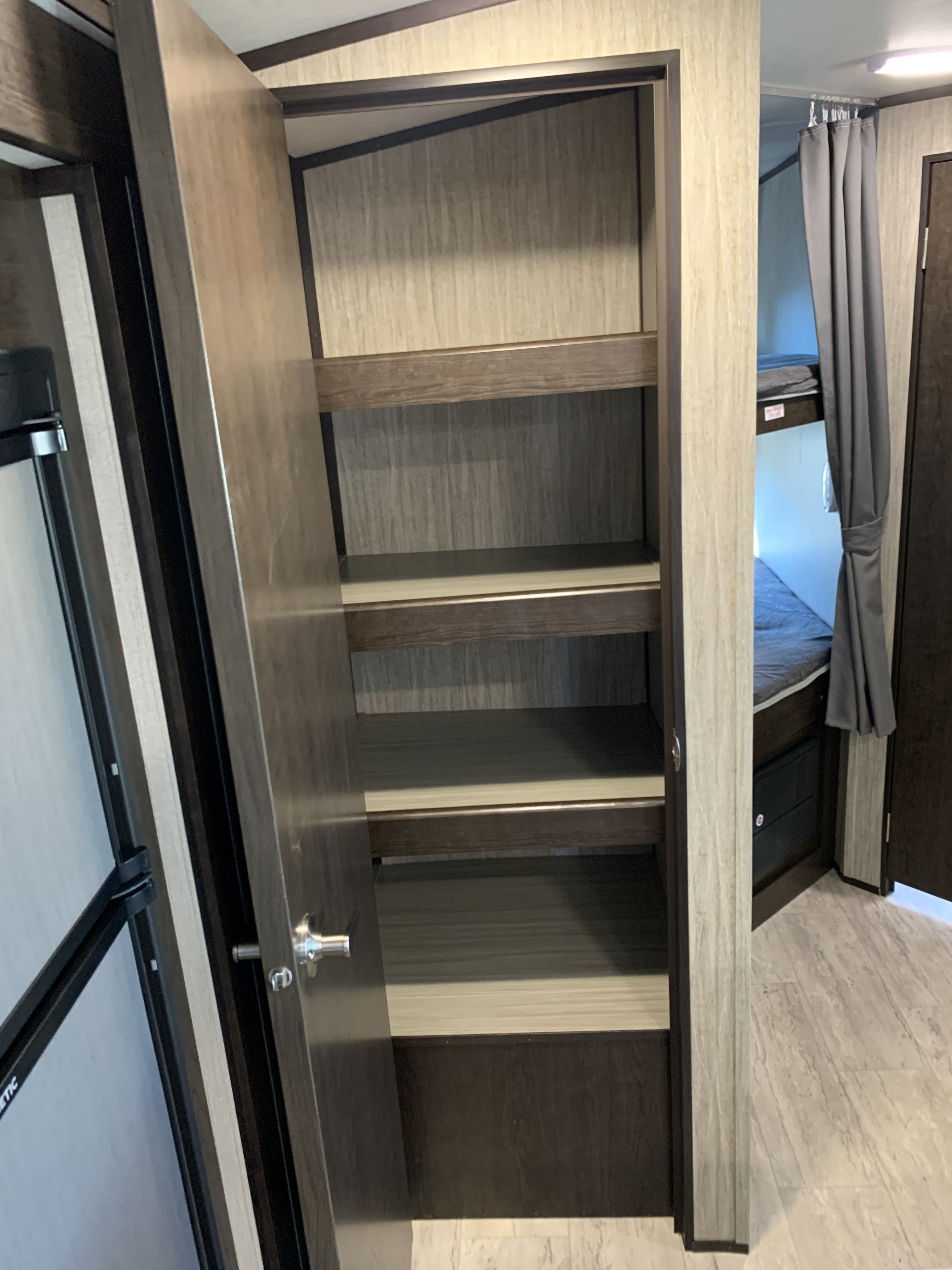 Explore an RV rental's interior: an open pantry with multiple shelves, a partial view of a refrigerator, and bunk beds with a privacy curtain.. Cruiser Rv Corp Shadow Cruiser 2019