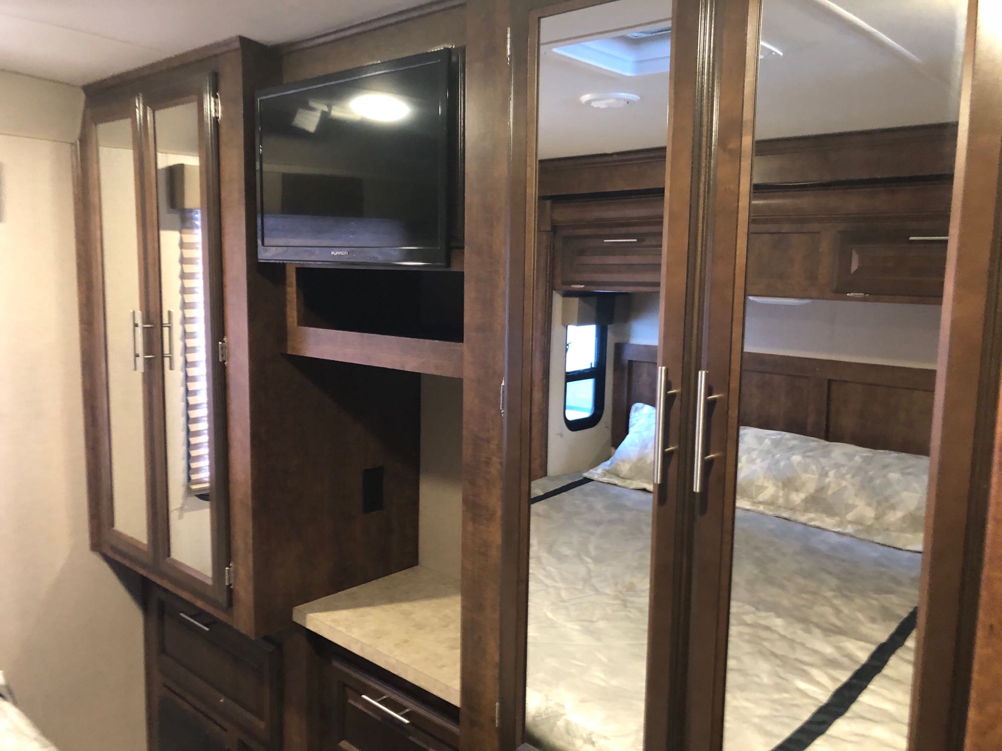 RV rental bedroom featuring dark wood cabinetry, a mounted TV, and mirrored closet doors reflecting the bed with patterned bedding.. Forest River FR3 2017