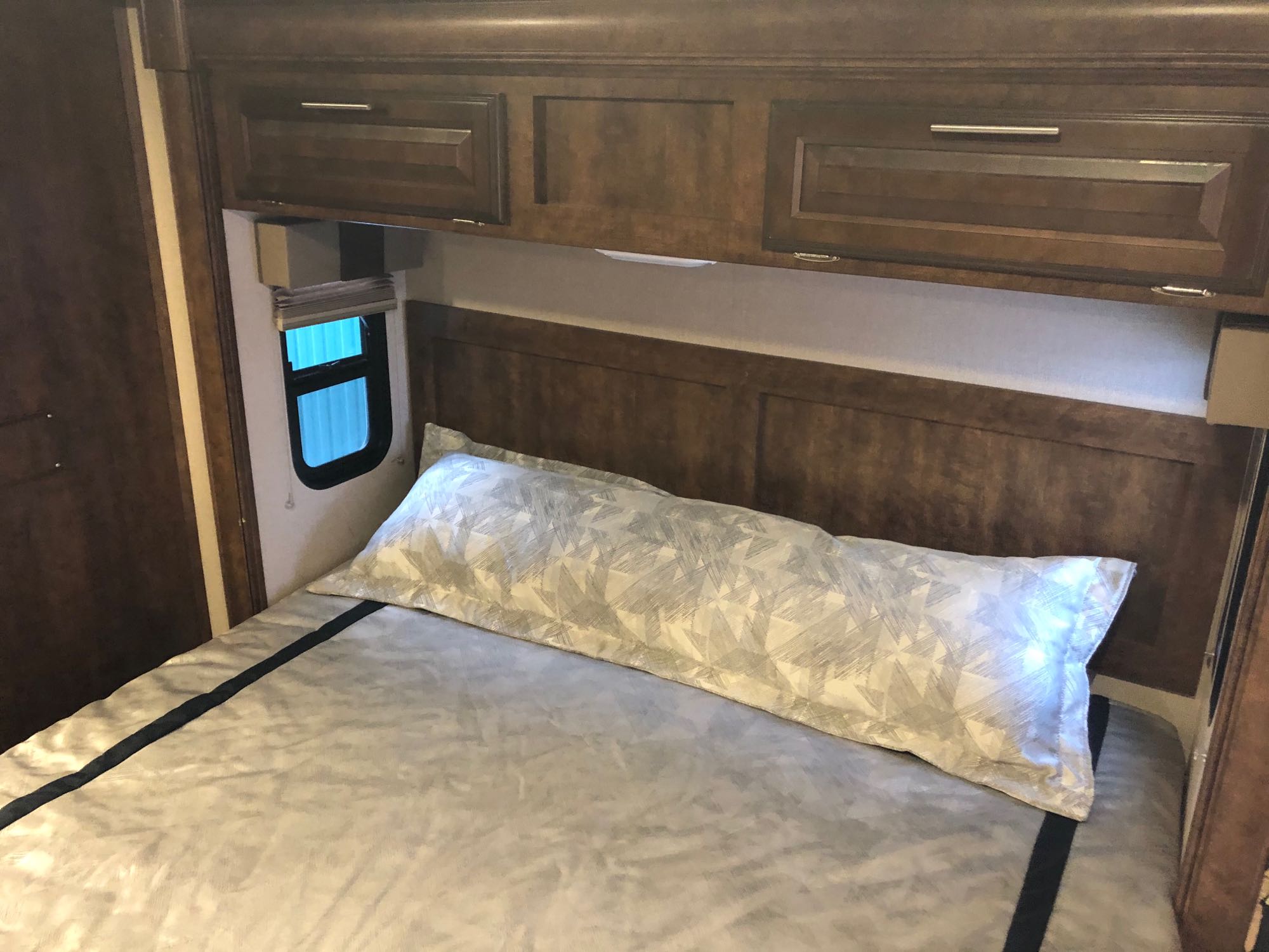 Compact RV bedroom showing a bed, patterned body pillow, and overhead cabinets. Great for your next rv rental trip!. Forest River FR3 2017