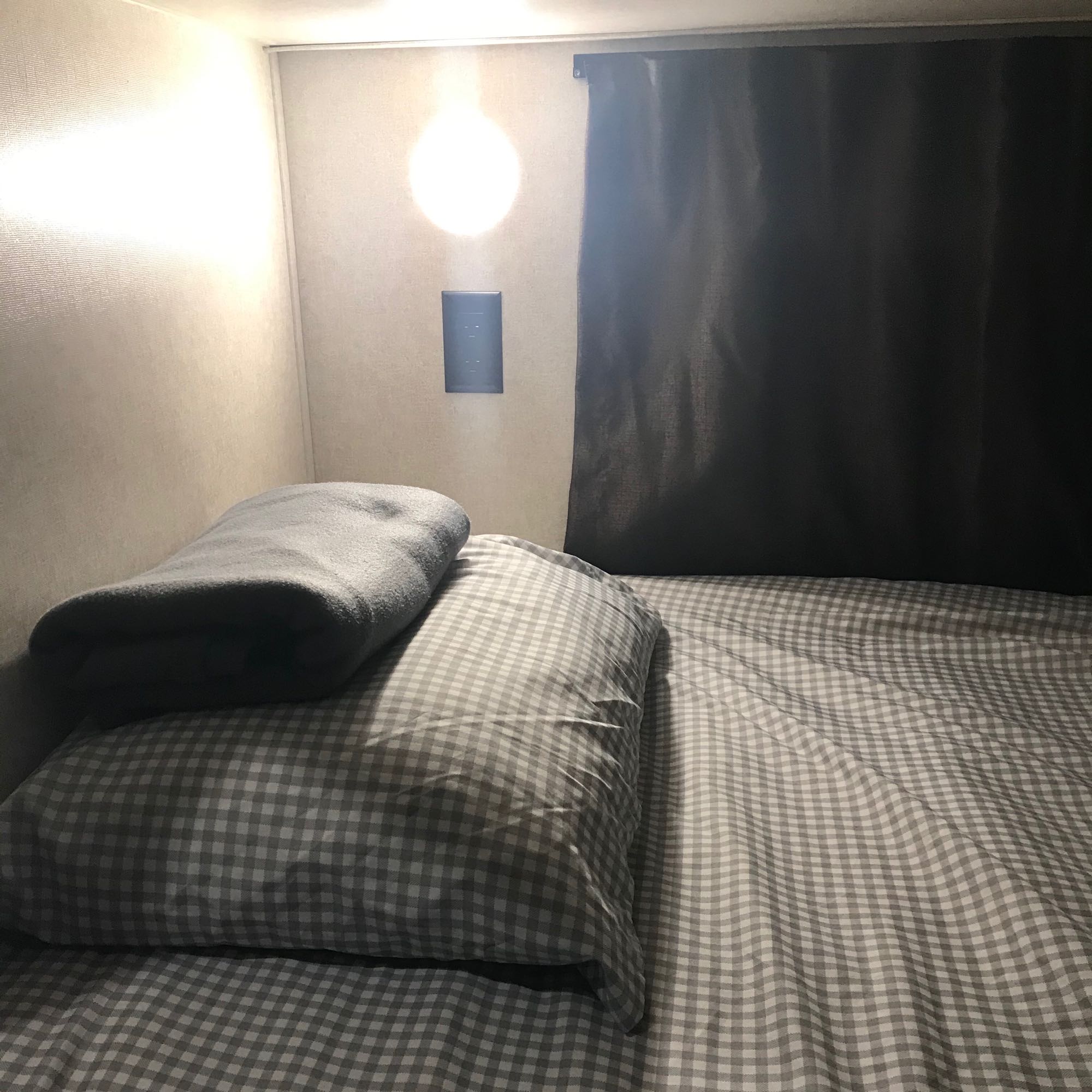 Cozy rv rental bed with gray checkered sheets, pillow, blanket, and wall light in a compact sleeping nook.. Jayco Jay Flight SLX 2019